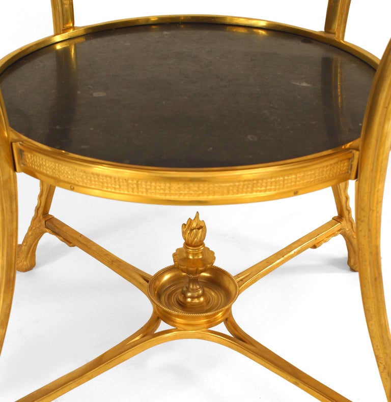 French Empire style bronze end table with 4 legs ending in lion heads holding rings with a round inset black marble top and shelf.