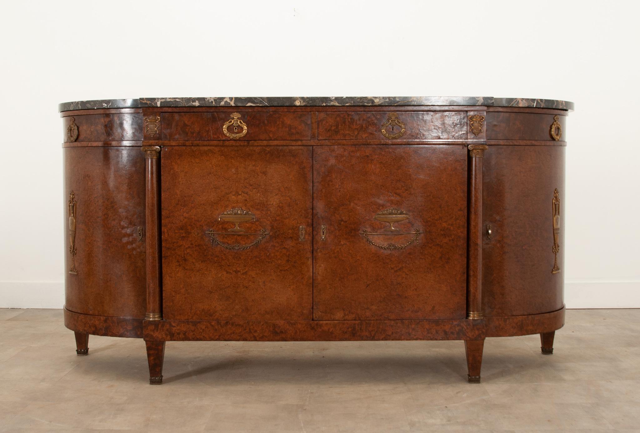 A gorgeous demilune enfilade crafted in France during the 1880s. This piece is all about the Empirically styled details and distinctive burl veneer. The original stunning marble top is shaped to fit the base. The apron houses four drawers with swan