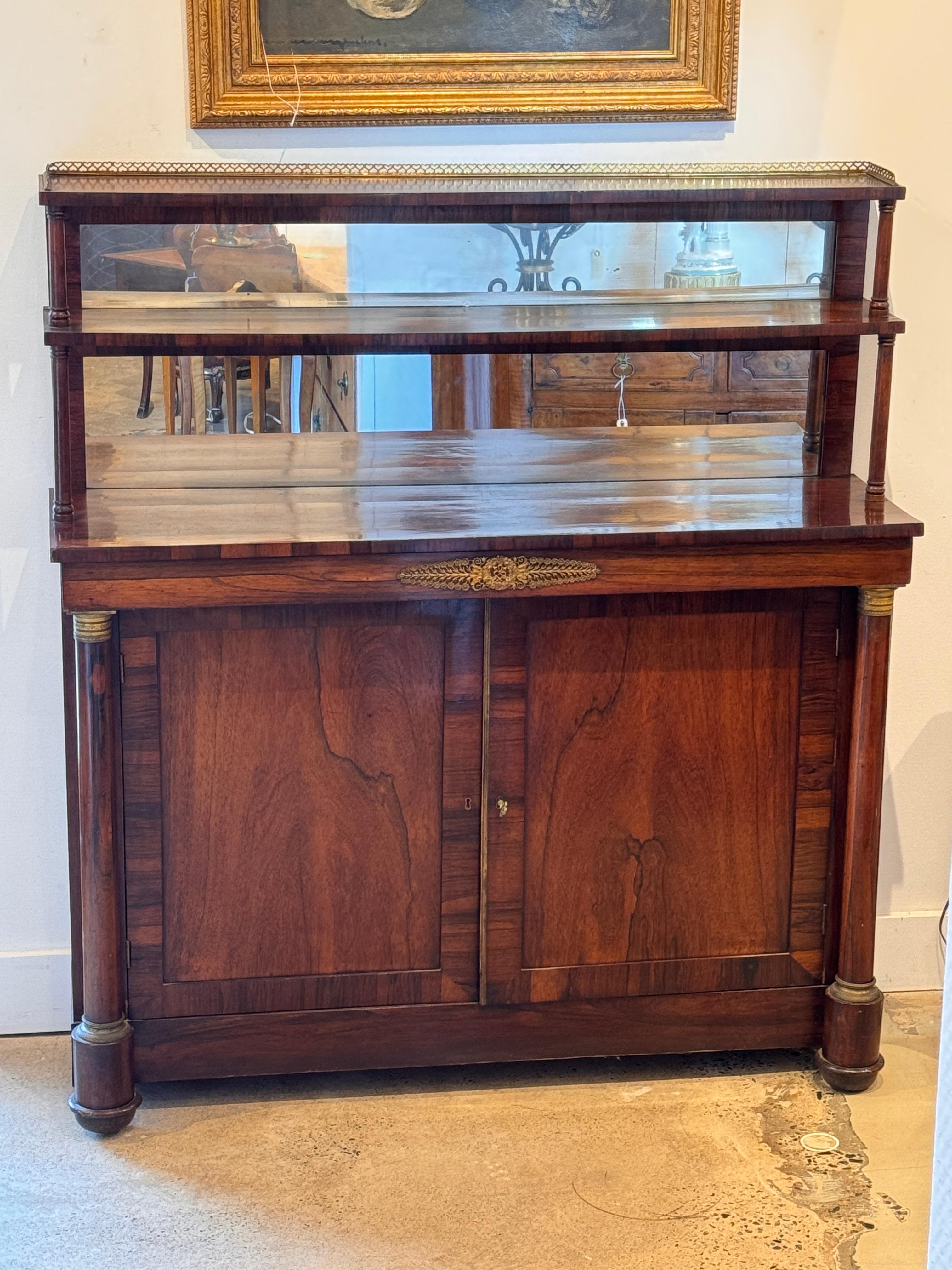 French Empire cabinet in rich mahogany, featuring a mirrored upper section with brass gallery and two tiers. The lower cabinet is flanked by columnar supports with gilt bronze capitals and mounts, and fitted with double doors opening to shelving.