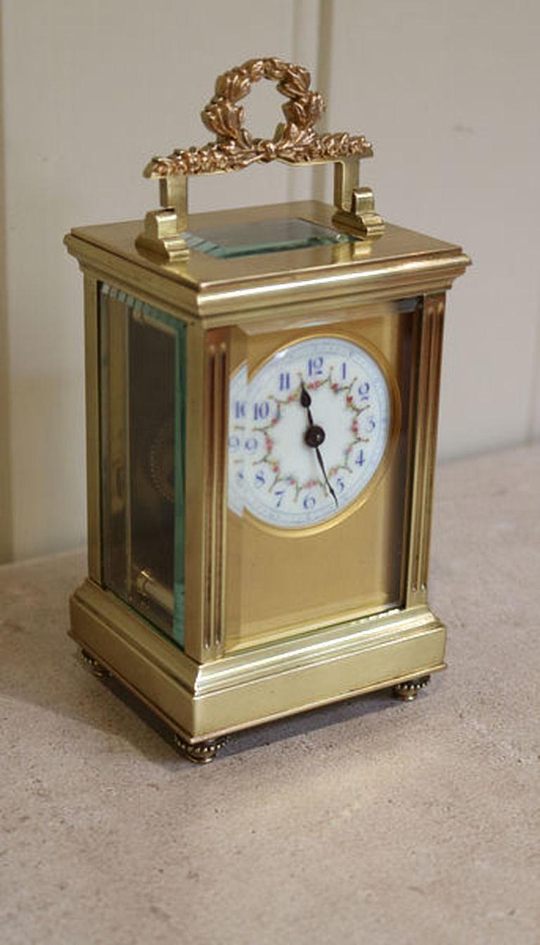A French Empire carriage clock, having a laurel leaf handle, reeded side columns and beaded round feet. The dial has a gilt dial mask and a hand decorated floral enamel dial with blue numerals. The 8 day movement has a cylinder platform.