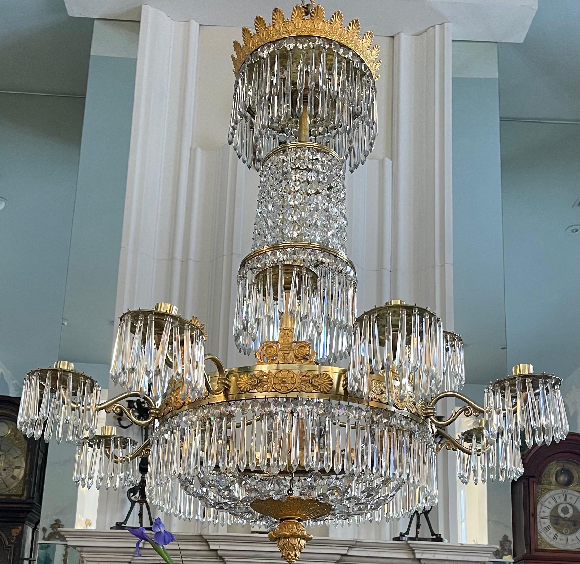 An elegant 12 arm French pendant from the 1st Empire Period. The lead crystal prisms are all original and have a subtle grey/purple hue. The chandelier resembles a four tier fountain. The two tone gold ormulu mounts depict Athenians and foliate