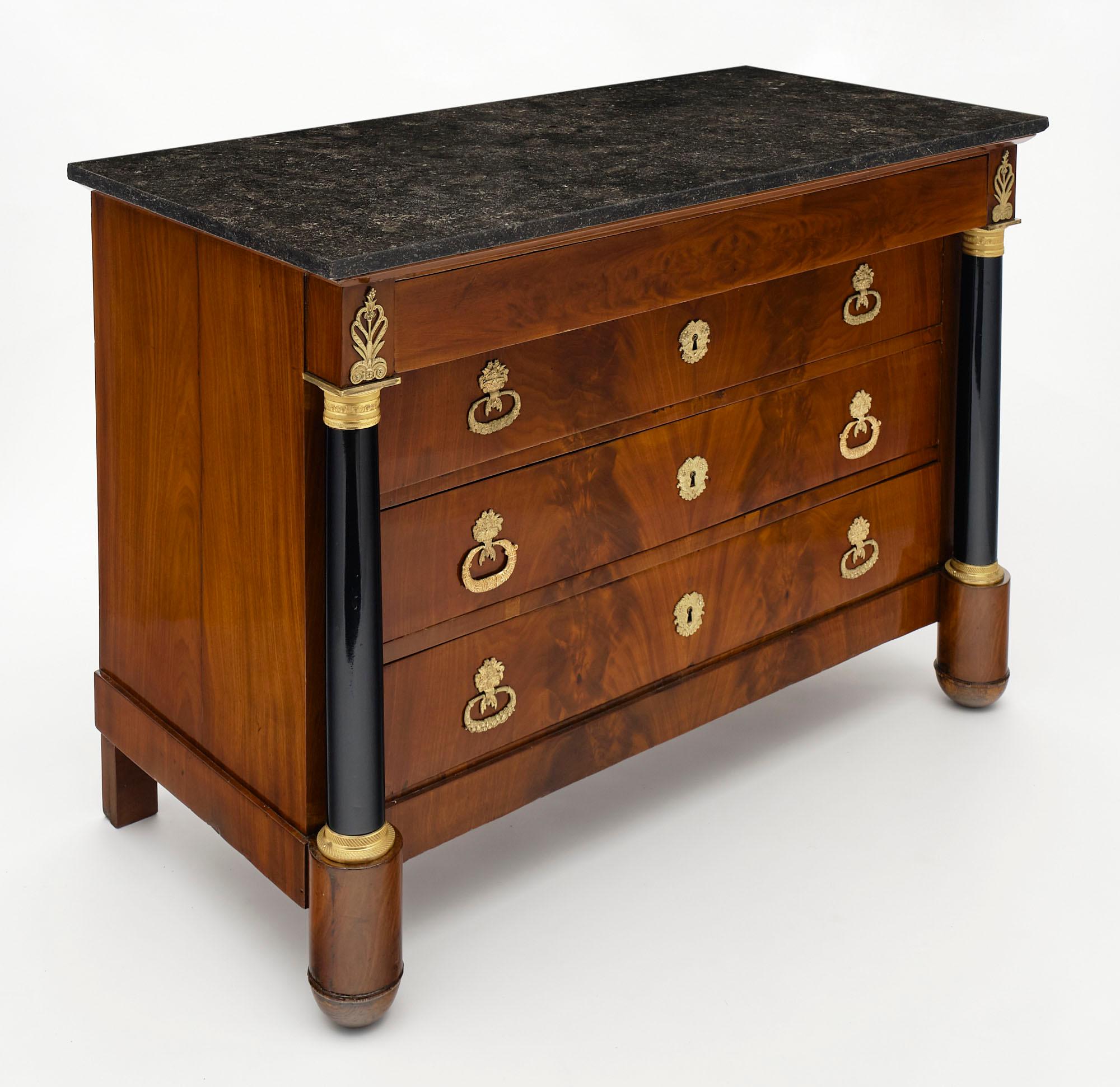 Chest of drawers or “commode” made of flamed mahogany in the French Empire style. This piece has ebonized columns and is finished in a lustrous French polish. There are four dovetailed drawers featuring finely cast gilt bronze hardware. Atop the