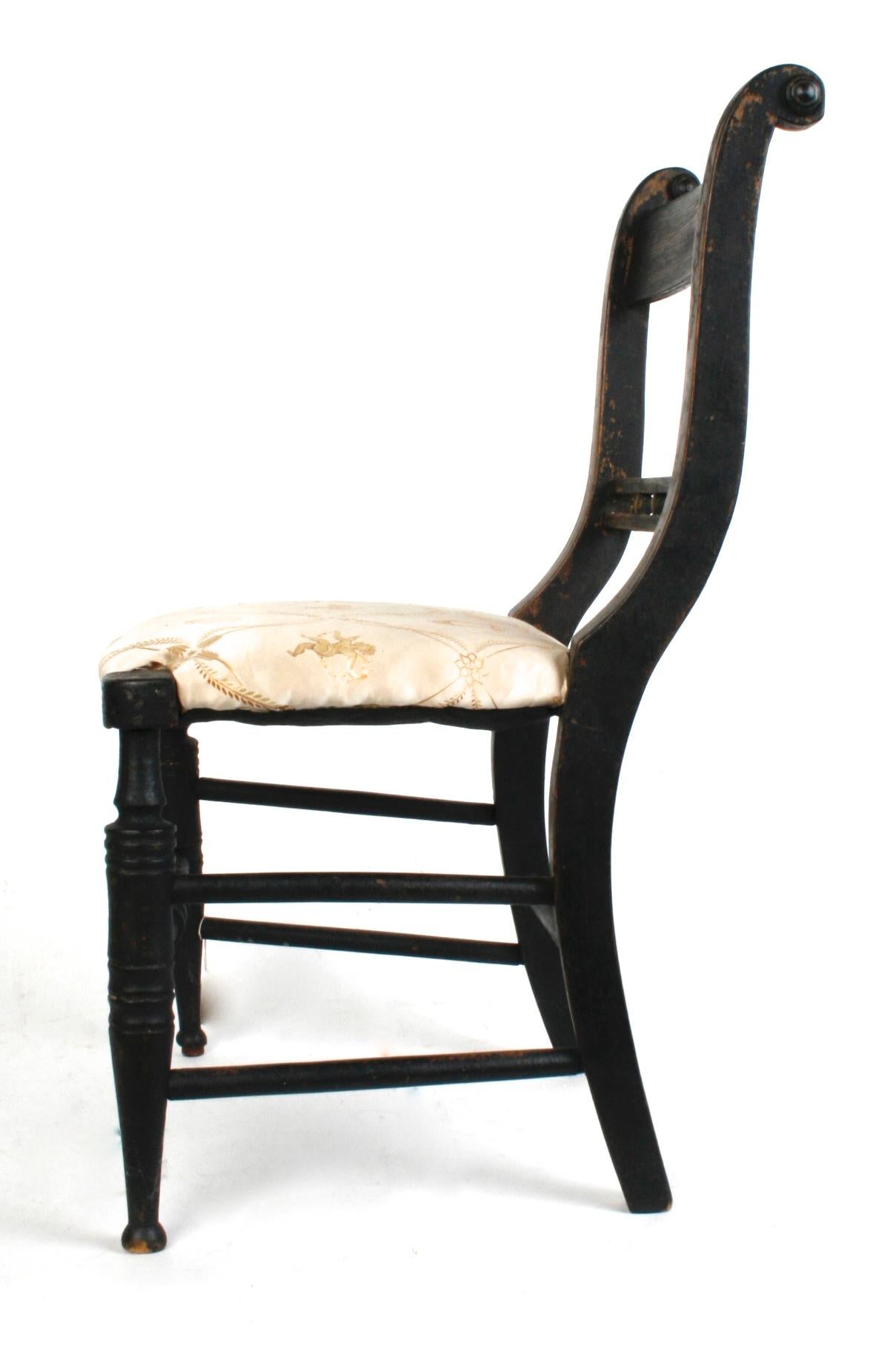 Black painted American Empire child's chair with upholstered seat, turned front legs and front stretcher. The back has a decorative double cross rail separated with five round wooden spacers. The chairs curved styles end in scrolls and turned caps.