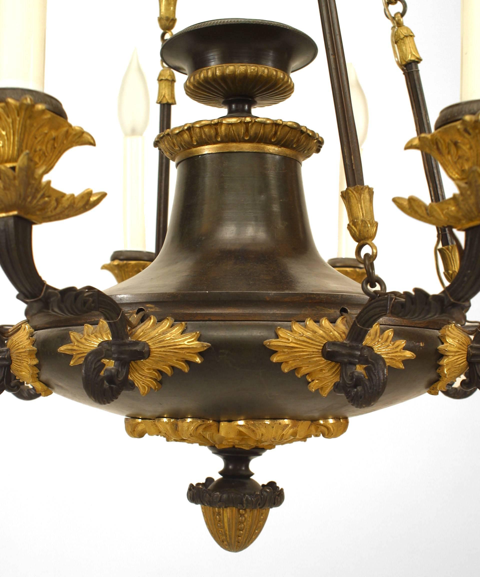 Französischer Empire-Kronleuchter (um 1820) aus Bronze und mit vergoldeten Verzierungen. Die 8 Arme gehen von einem runden Kranz mit Eicheltropfen aus und werden von 4 Ketten mit Blättern getragen.
