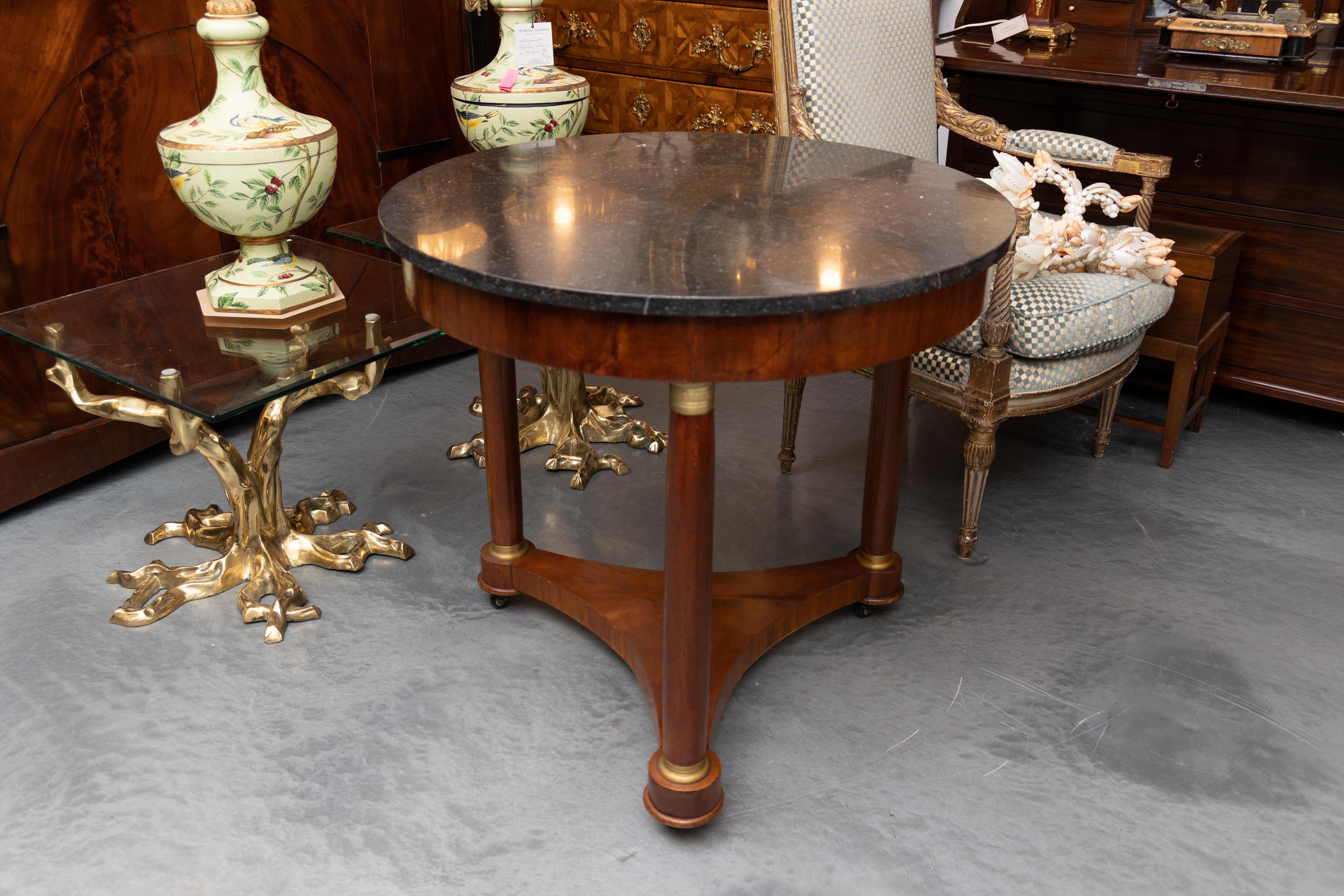 This is a classic French Empire mahogany circular center table, the black marble top over a wide frieze supported by round, slightly tapering columns with brass collars, joined by a full mahogany tripartite base, circa 1830.