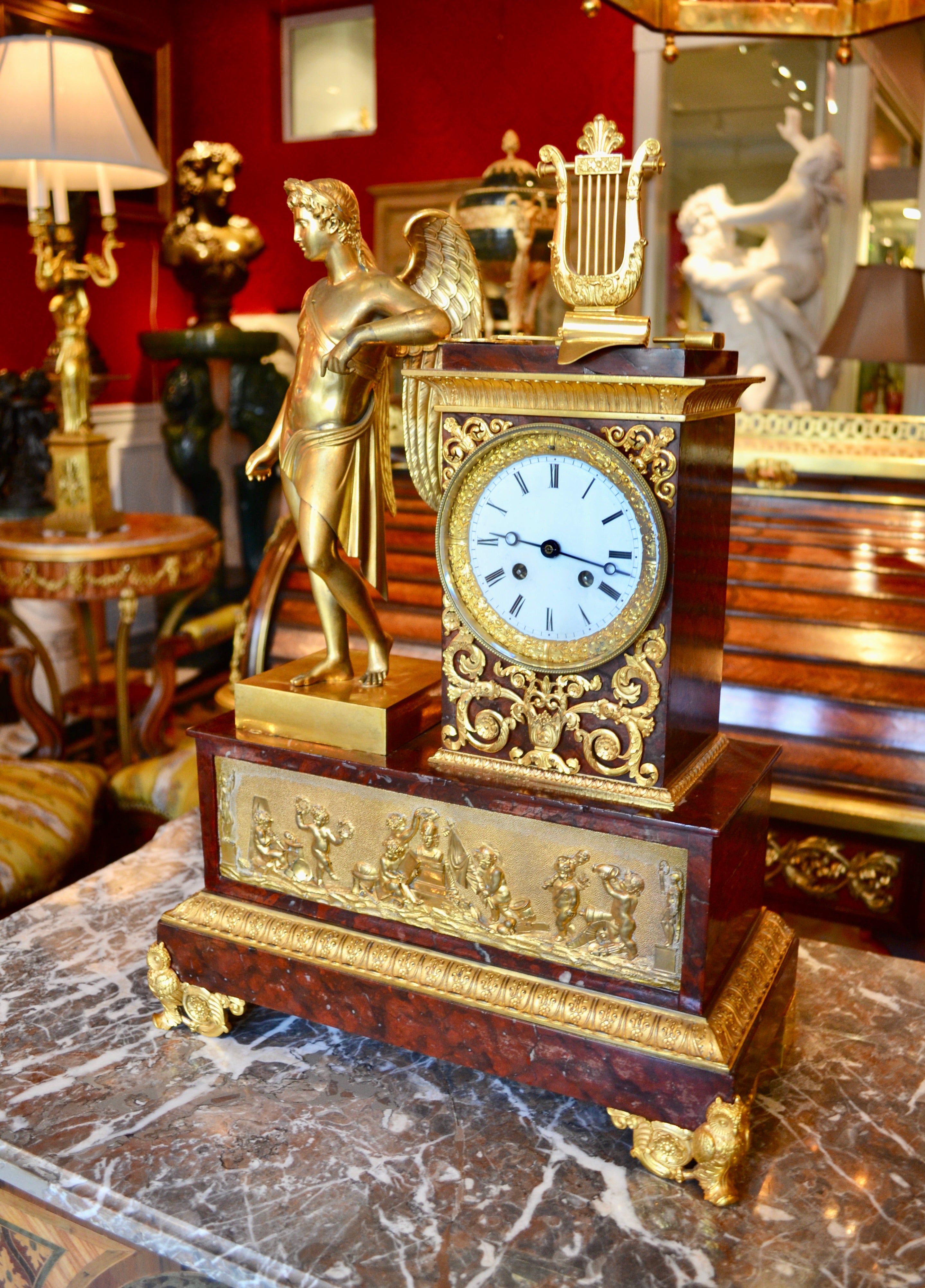 A gilt bronze and griotte marble French Empire clock depicting  Apollo Greek God of Music Art Literature and Sciences. The clock shows a a gilt bronze winged figure of Apollo leaning against a griotte marble altar pedestal decorated with gilt bronze