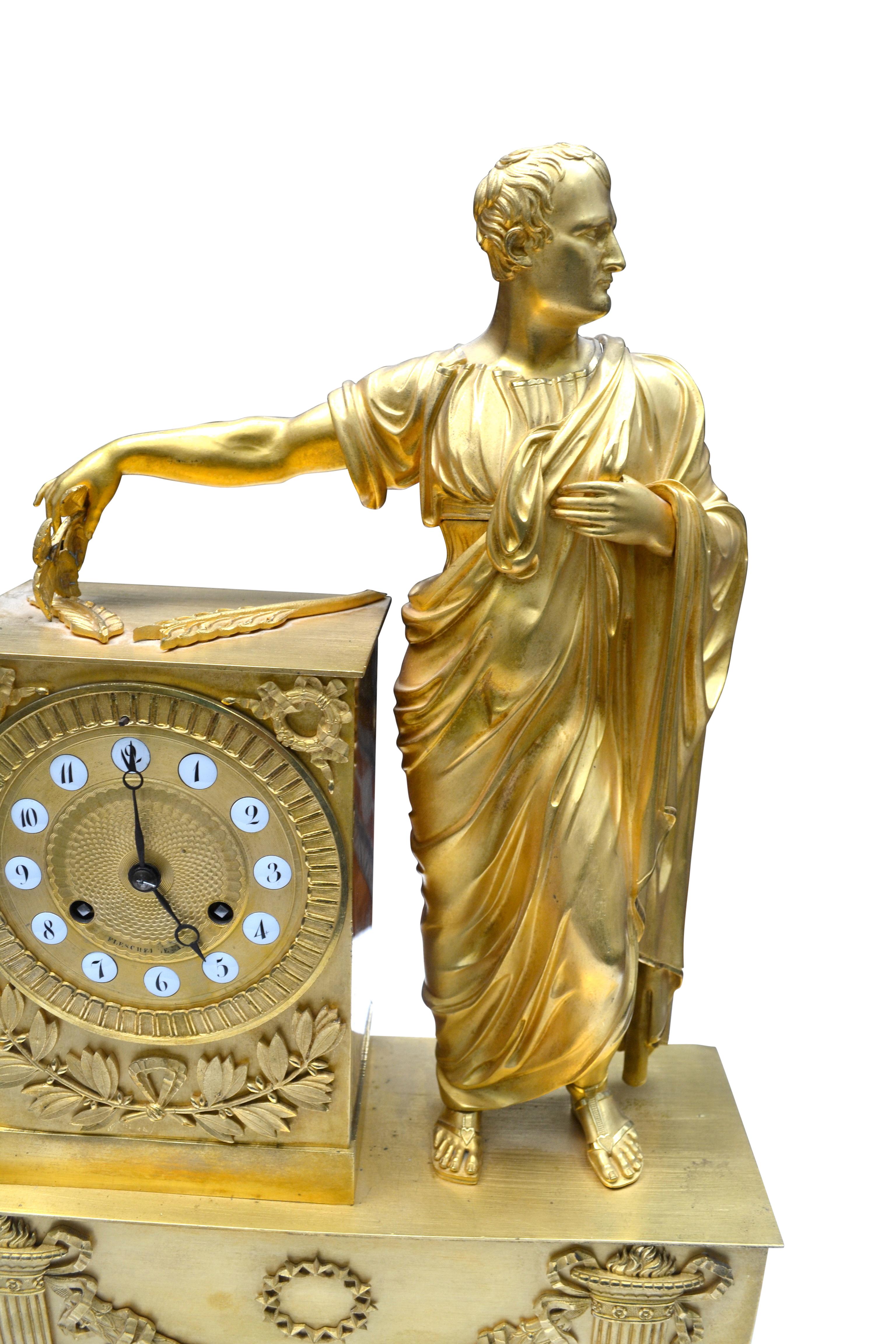 A finely chased and mercury gilded French Empire mantel (fireplace) clock showing a standing Napoleon dressed as Caesar holding leaves in his extended left hand. The clock plinth is decorated with wreath and laurel leaves; the lower rectangular base