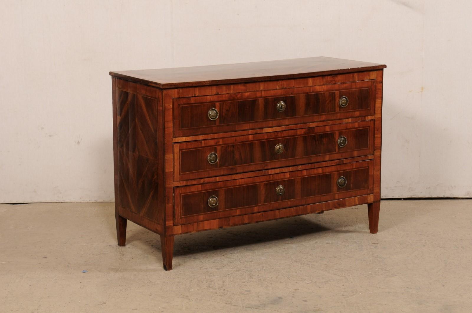 A French Empire commode with beautiful inlay and book-match veneers, from the early 19th century. This antique chest from France features a rectangular-shaped, book-match veneer top, with banding inlays defining the perimeter. The case below houses