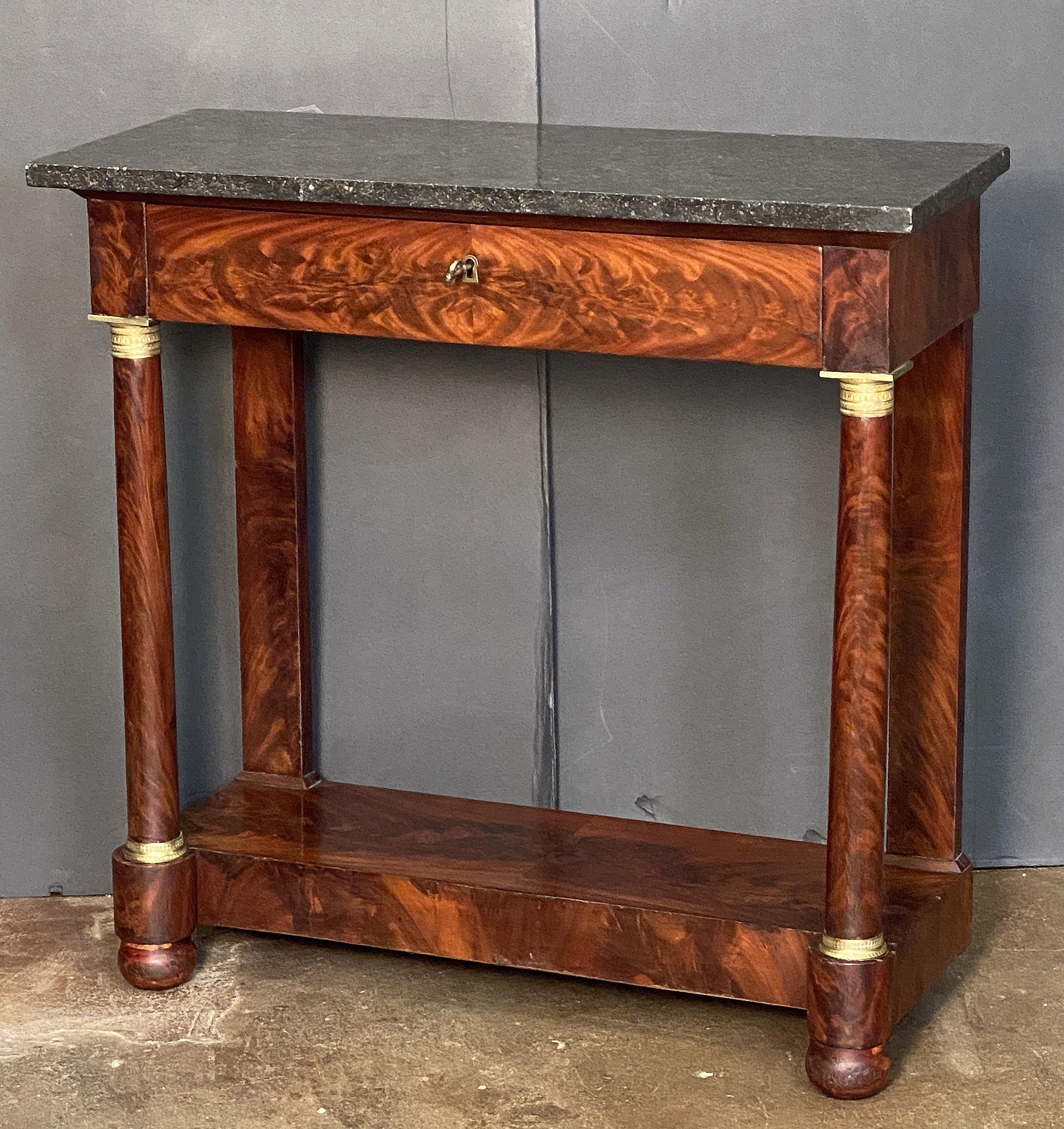 A handsome French Empire console table of fine proportions, featuring a rectangular figured marble top, set upon a frieze of flame mahogany with one long drawer, the drawer with brass escutcheon and key, over a base with two facing column supports