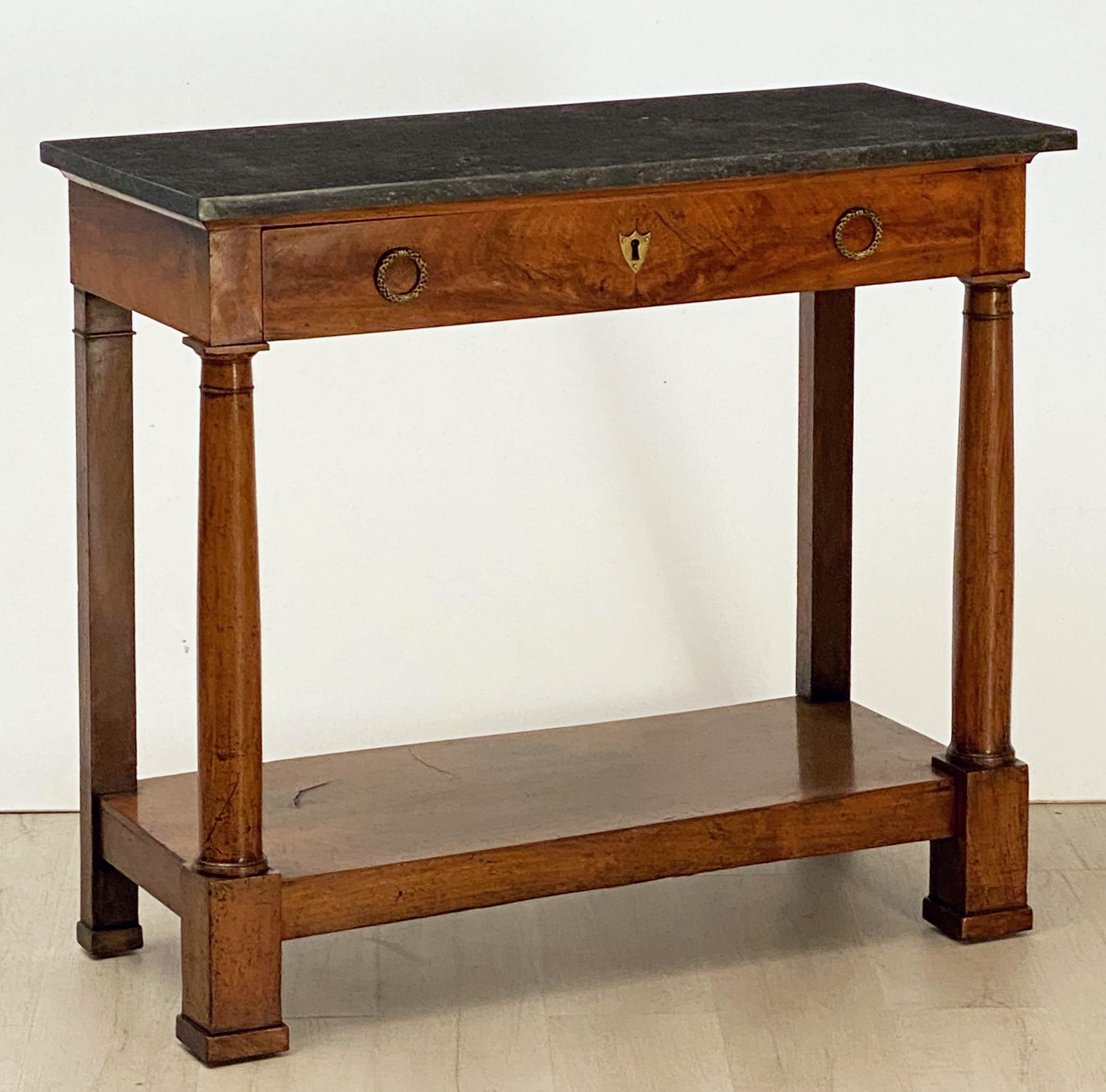 A period French Empire console table of mahogany of fine proportions, featuring a rectangular figured marble top set upon a frieze with one long drawer, the drawer with brass escutcheon and pulls, over a base with two facing turned column supports,