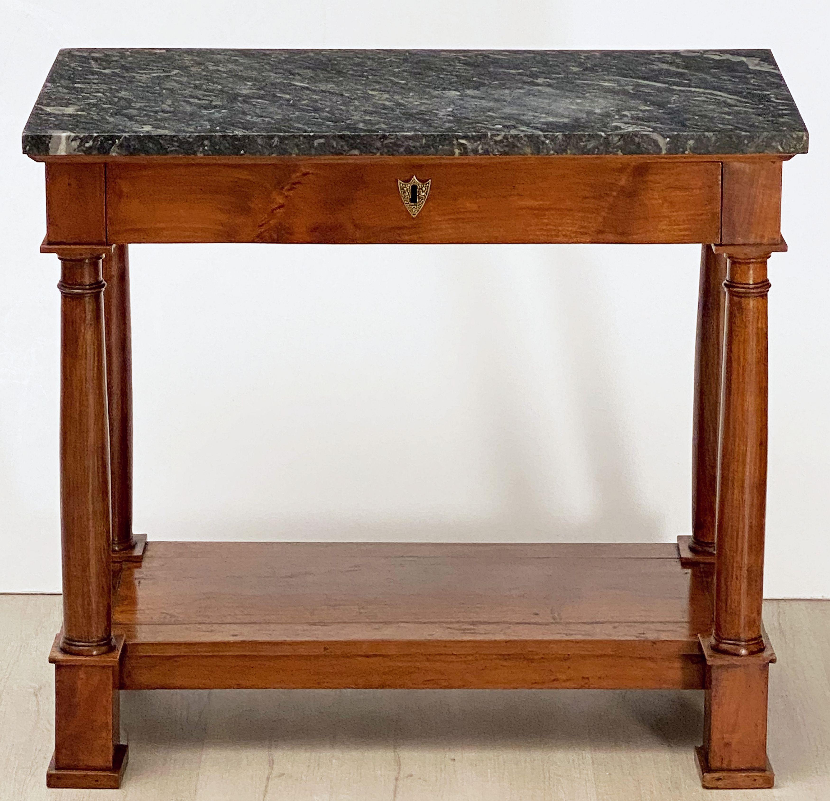 A period French Empire console table of mahogany of fine proportions, featuring a rectangular figured marble top set upon a frieze with one long drawer, the drawer with brass escutcheon, over a base with four turned column supports, bottom shelf,