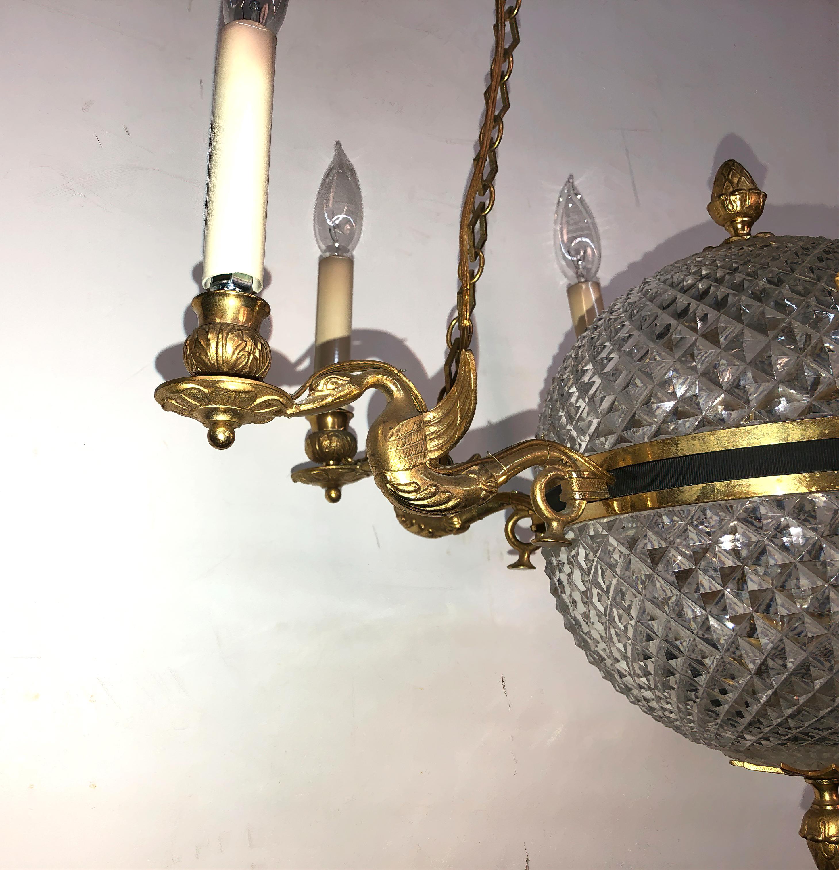 A French Empire cut glass crystal ball chandelier with four bronze swan form arms, acorn finials and palmette mounted canopy.