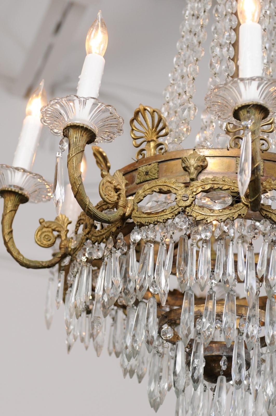 A French Empire style bronze and crystal eight-light chandelier from the early 20th century, with palmettes and acanthus leaf motifs. This cut crystal, eight-light chandelier has exquisite detail embellished with cut crystal prisms. A crown with