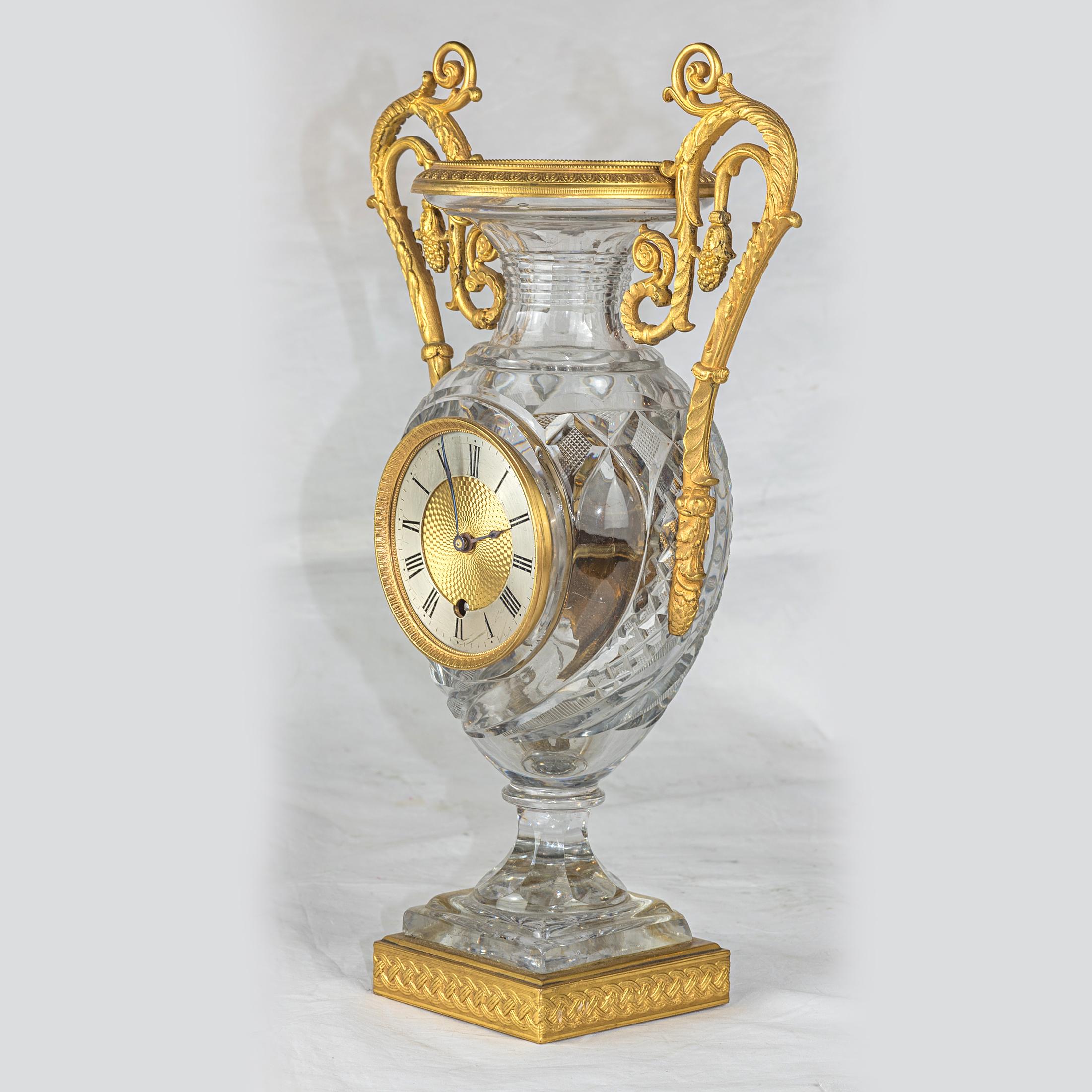 Pendule Médicis en cristal taillé en forme de vase, montée en bronze doré. Deux poignées dorées avec feuillage.

Origine : Français
Date : vers 1810
Dimension : 14 x 8 3/4 x 4 1/4 pouces