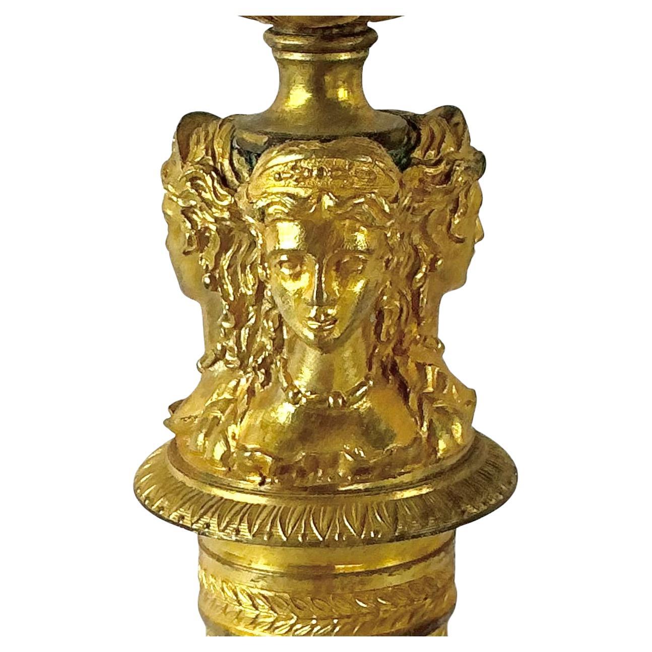 Pair of French Empire Doré Bronze Candlesticks. These candlesticks feature a fluted and diamond-patterned shaft rising from a circular molded base with guilloché border. The upper section is adorned with three finely cast maiden's busts and paw