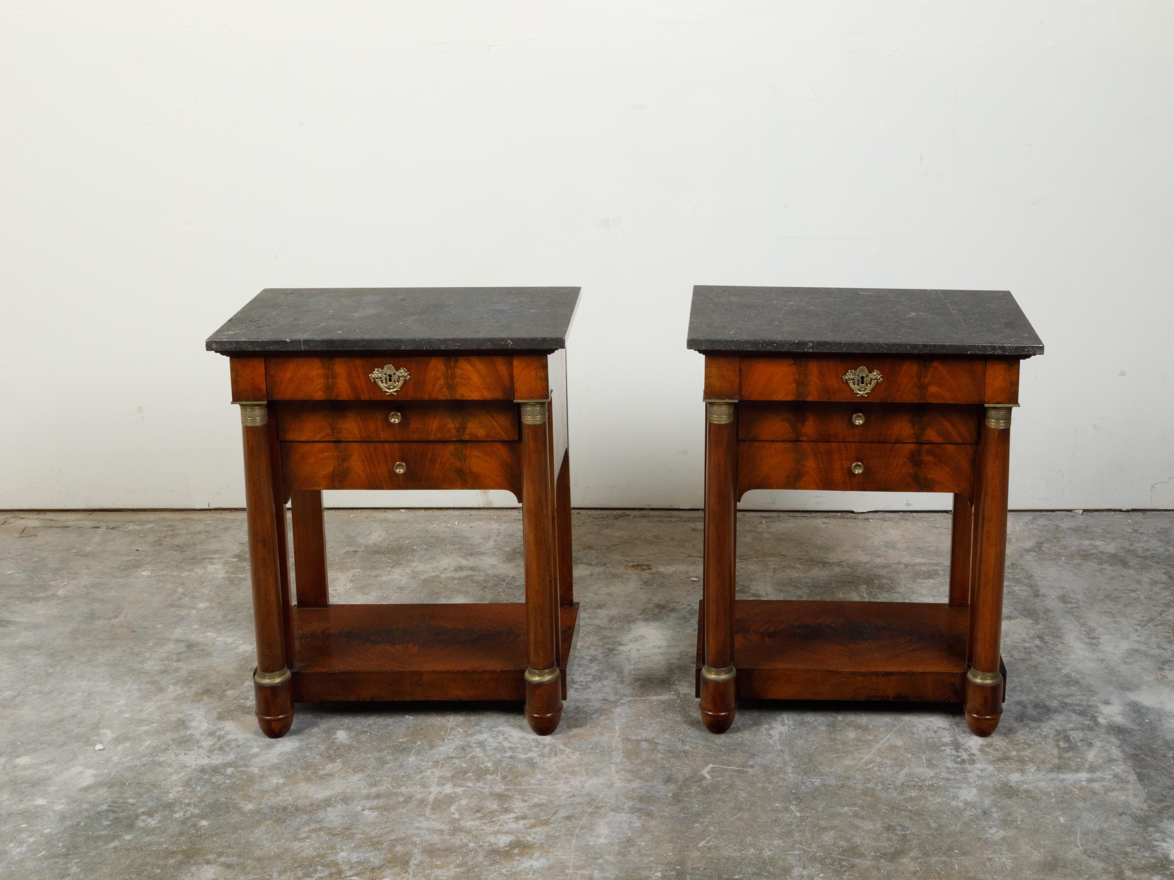 A pair of French Empire period walnut veneered console tables from the early 19th century, with dark grey marble tops, bronze mounts and two drawers. Created in France during the early years of the 19th century, each of this pair of console tables