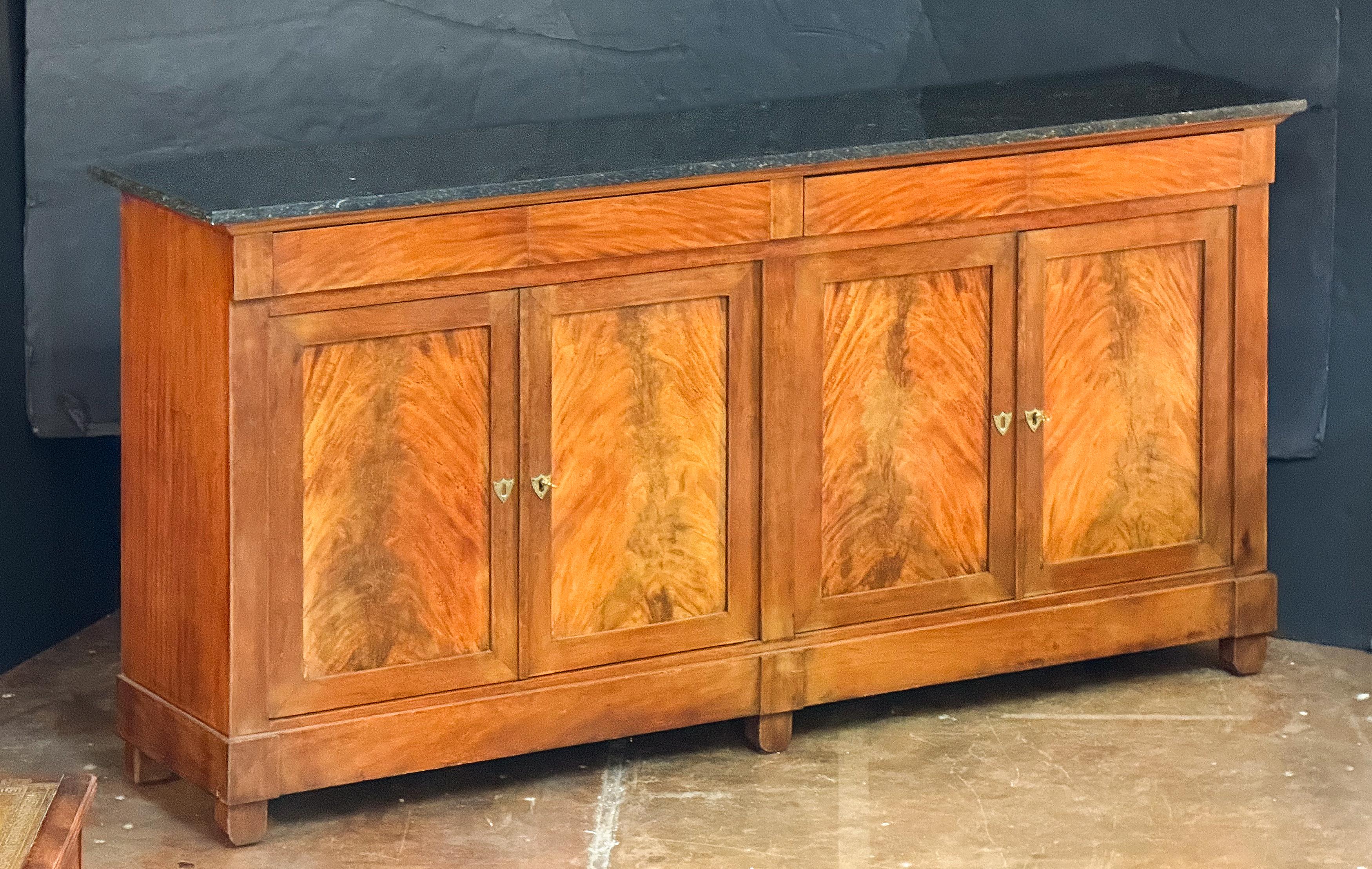 An elegant French Empire enfilade or sideboard console server of flame mahogany with original marble top, from the 19th century, featuring a frieze showing four drawers with reflecting veneers on each drawer front, over two pairs of locking cupboard