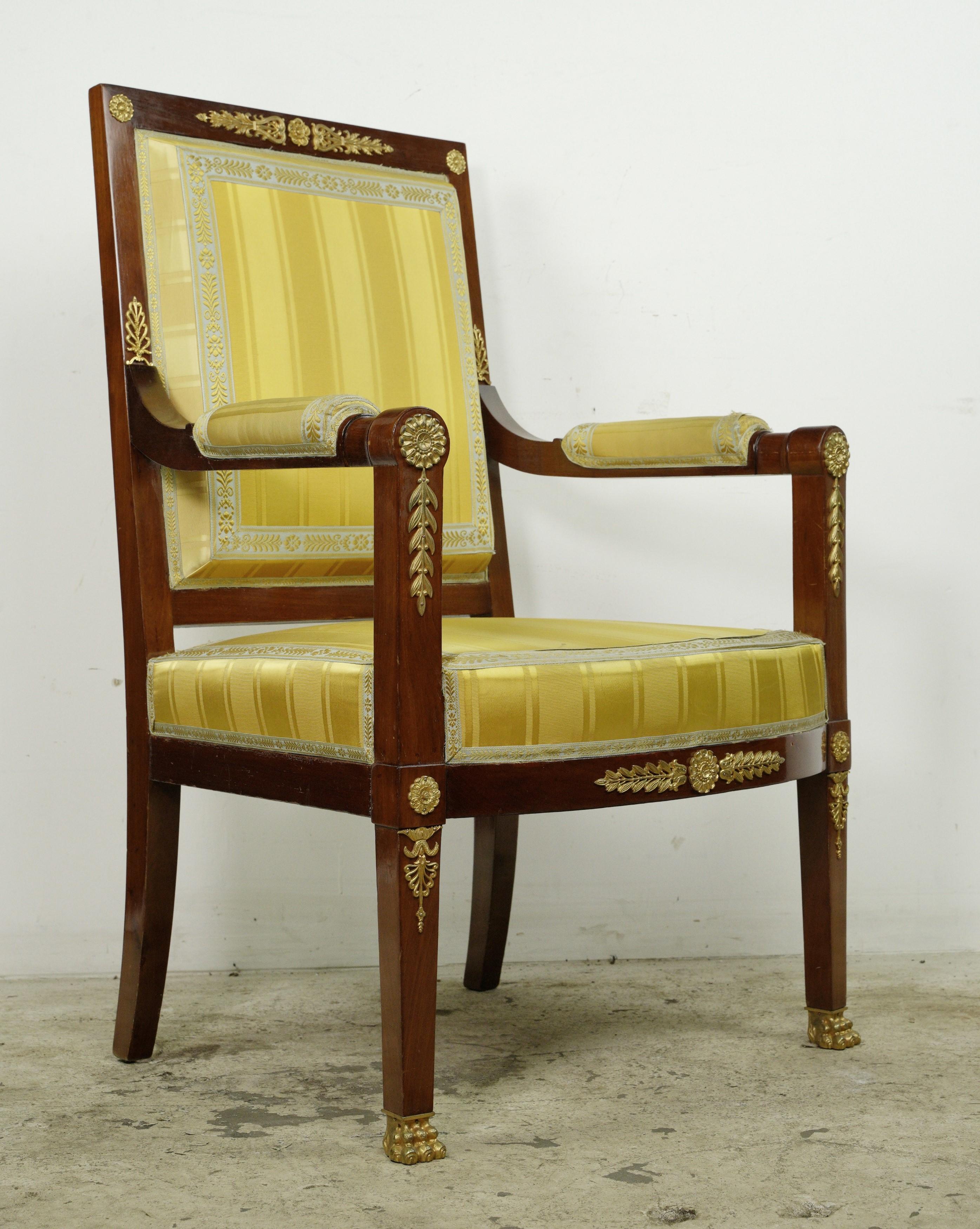 This piece was procured from an esteemed estate located in Greenwich, Connecticut. This armchair features a mahogany frame adorned with gilt brass accents, showcasing intricate scroll and foliate details. The yellow striped upholstery adds a touch
