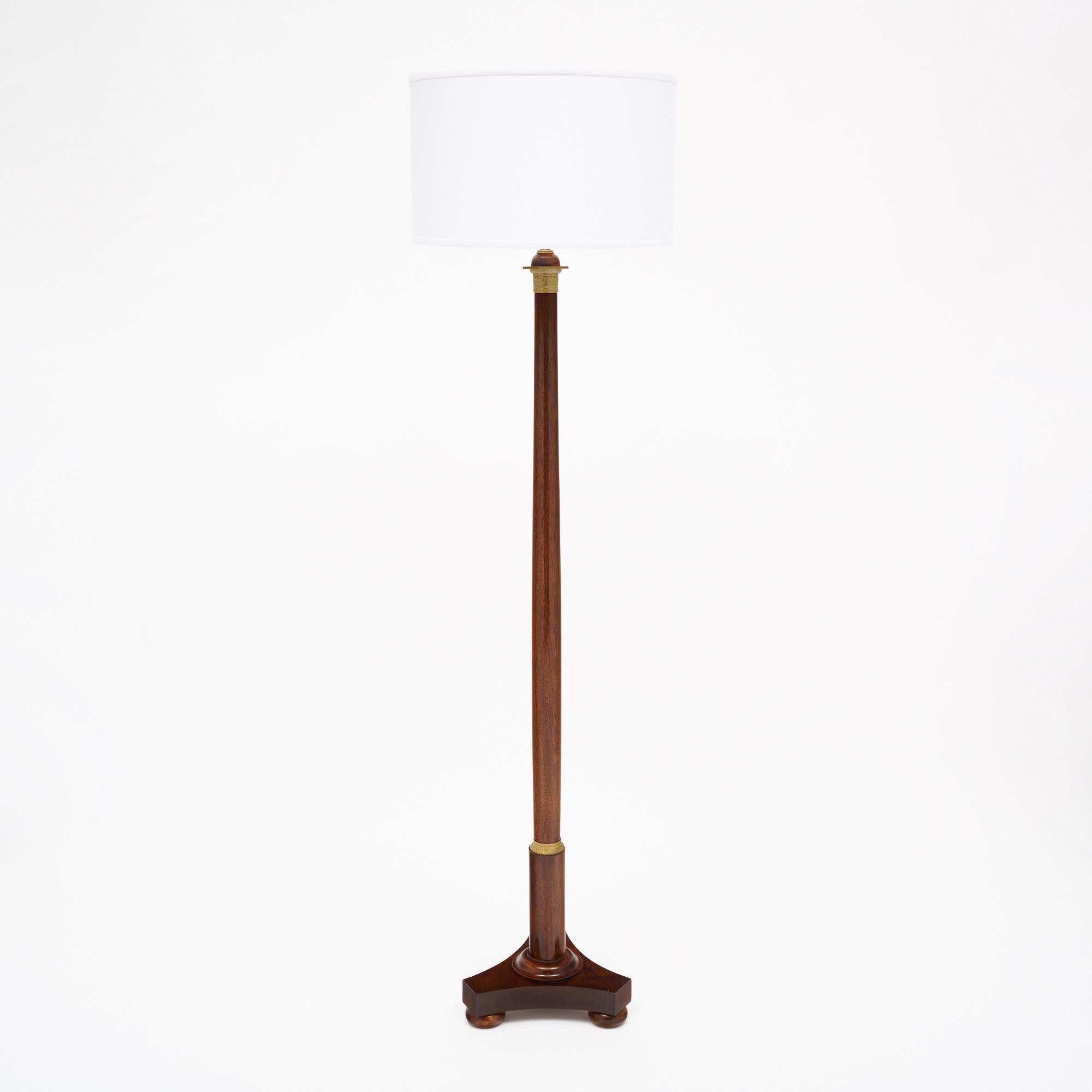 French floor lamp of solid flamed Mahogany finished with a lustrous museum quality French polish and finely cast gilt bronze decorative rings. This floor lamp features a tripod base. The shade is 11” in height and 18.5” in diameter. The height of