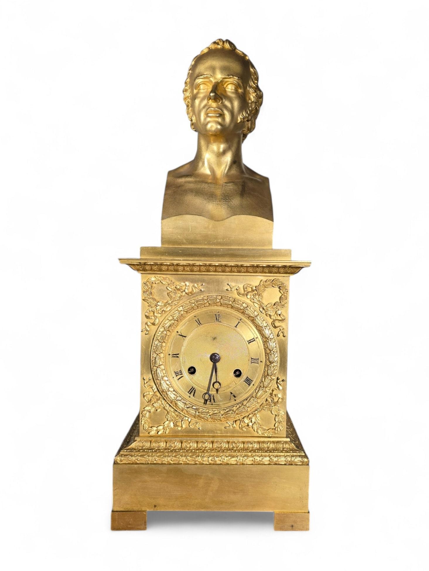 An elegant French Empire-style mantel clock crafted in gilded bronze, featuring a classic bust of a gentleman as its central decorative element. This timepiece exemplifies the refined artistry and luxurious design characteristic of the Empire