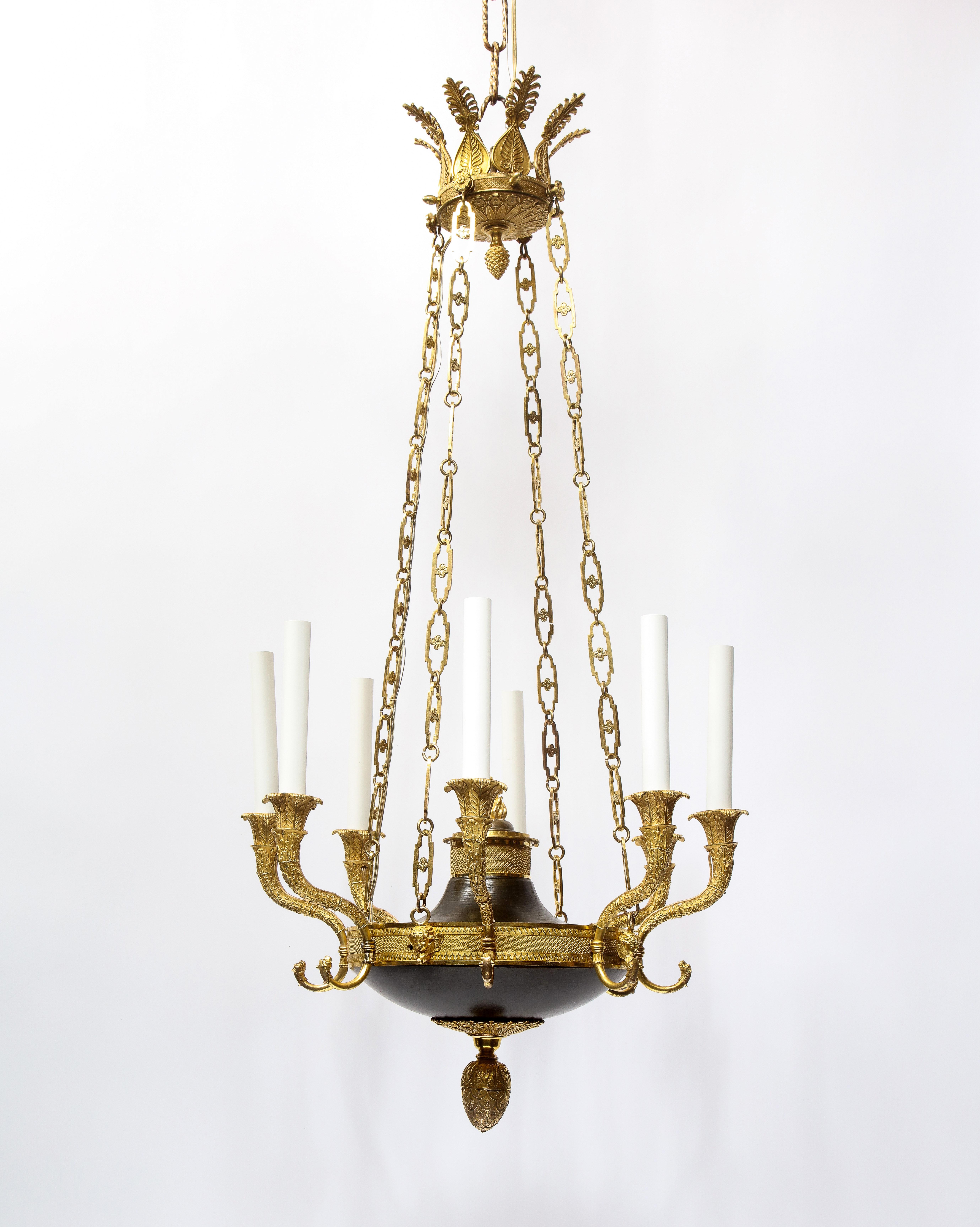 Questo lampadario è un lampadario a otto luci in stile Impero francese realizzato in  XIX secolo in bronzo patinato e dorato. Il design presenta elementi classici del periodo dell'Impero, come teste di leone, maschere femminili alate e motivi di