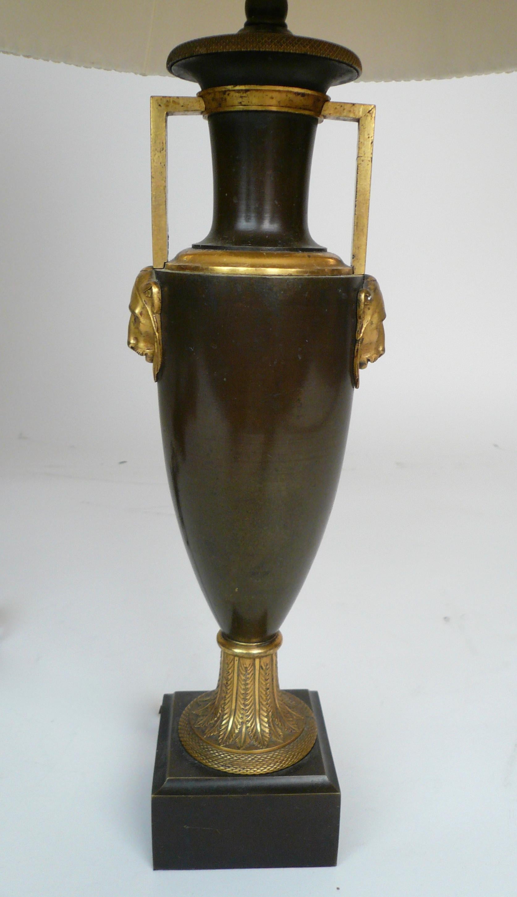 This detailed bronze urn form lamp features gilt bronze highlights including lepard head handles, and acanthus leaves.