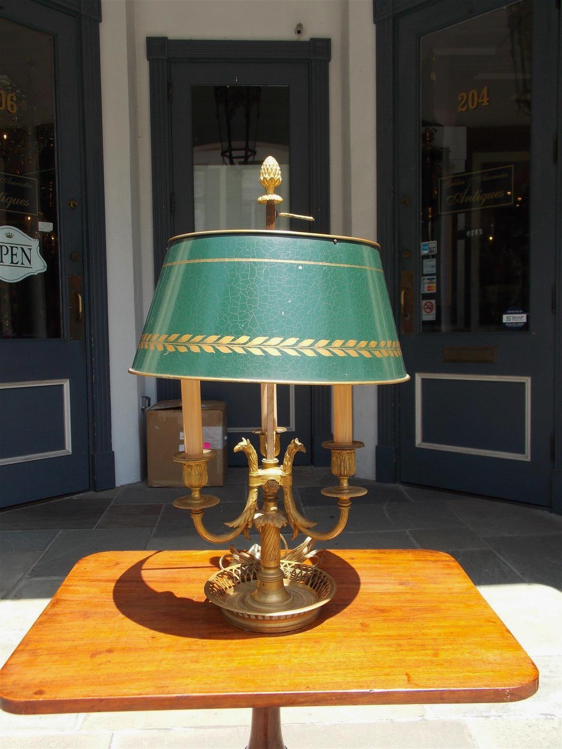 French Empire gilt bronze bouillotte lamp with three scrolled arms, interior griffon heads, telescopic tole shade with pineapple and feather finial, and resting on the original circular pierced gallery hand chased base. Early 19th century.