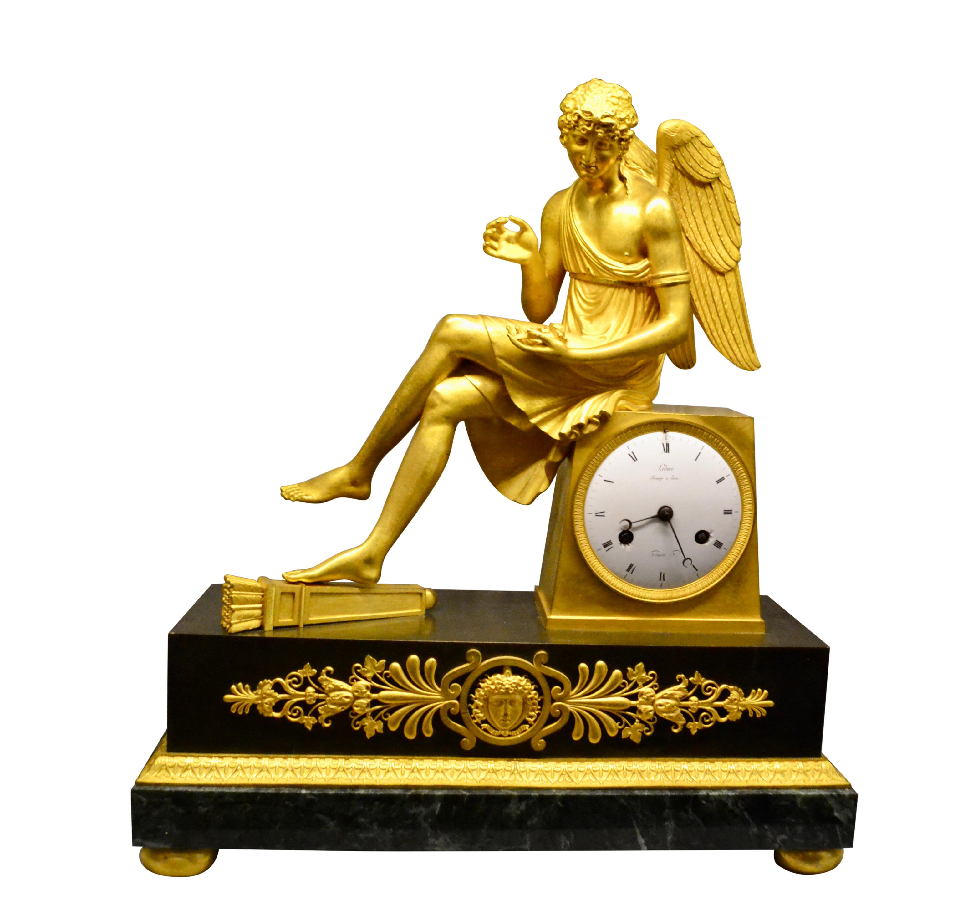 Finest quality period French Empire clock depicting a seated winged cupid holding a rose; the case in gilt and patinated bronze. The clock show a gilt cupid sitting cross legged on the clock plinth, with one foot resting on a quiver and his left