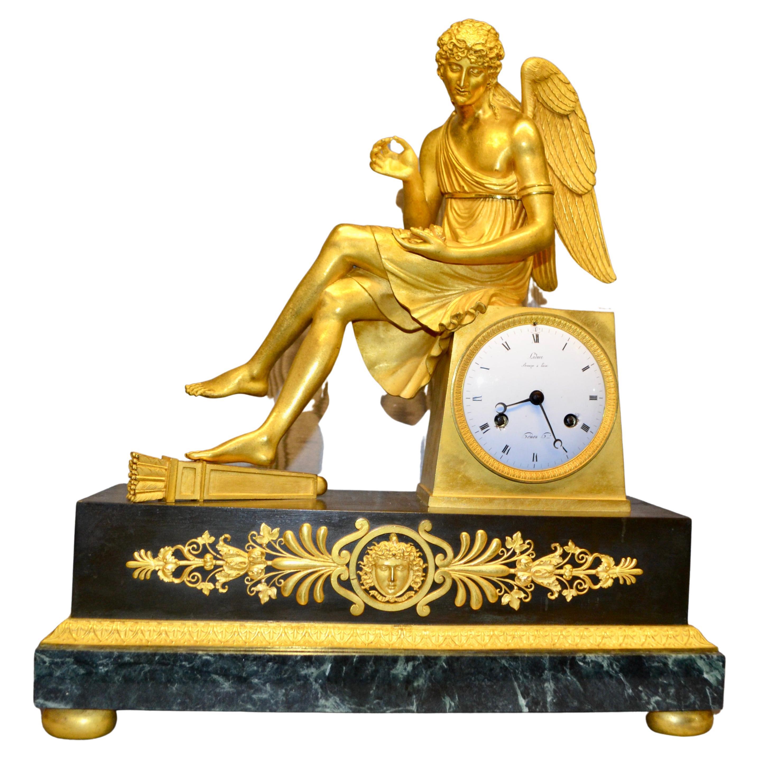 Horloge Empire française en bronze doré et marbre représentant Cupidon assis tenant une rose