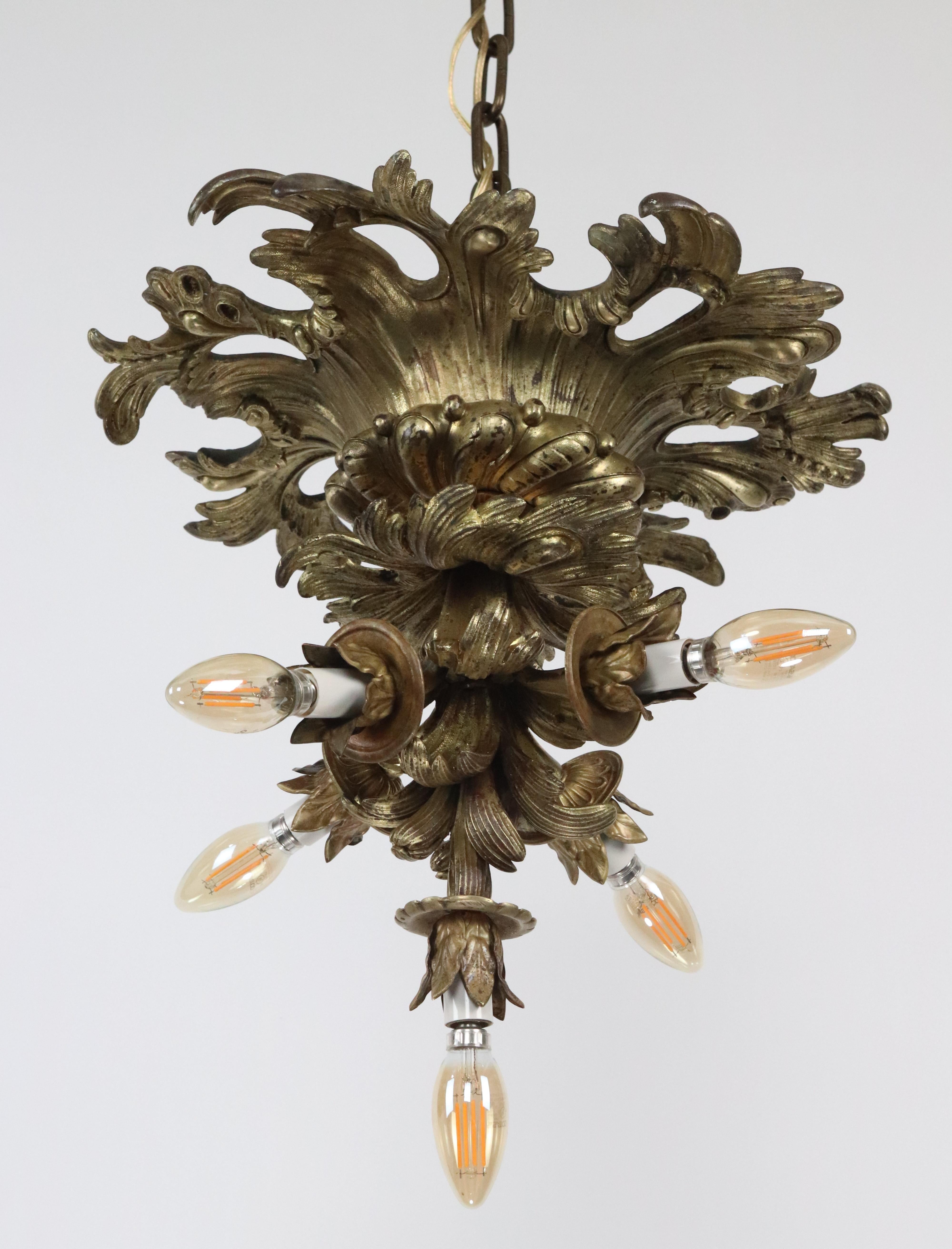 Lampadario in stile Impero francese realizzato in bronzo con finitura dorata. Ha bracci multipli che si estendono da un motivo fogliare centrale, ognuno dei quali sostiene una lampadina a vista, ed è sospeso da una catena. Questa lampada richiede