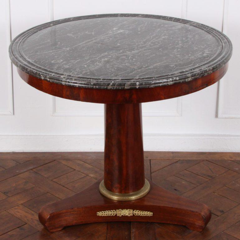 A mahogany, 19th century, French Empire centre table or ‘gueridon’ with a simple geometric three-sided base below a tapering column support and retaining the original marble top with a complex hand-shaped edge, circa 1835-1840.



    