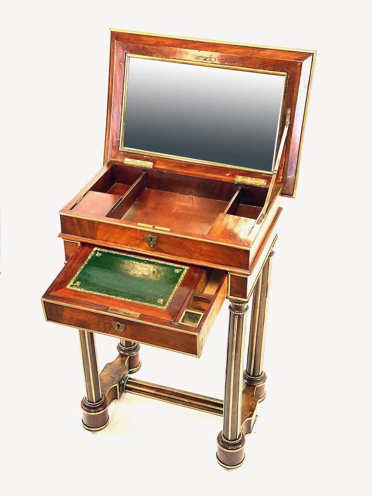 Mahogany Empire style Military officers campaign desk. Flip top fitted with mirror raises to reveal open storage. One drawer lined with tooled leather and one lead inkwell. Turned legs fluted with brass mounts throughout. Later half of the 19th
