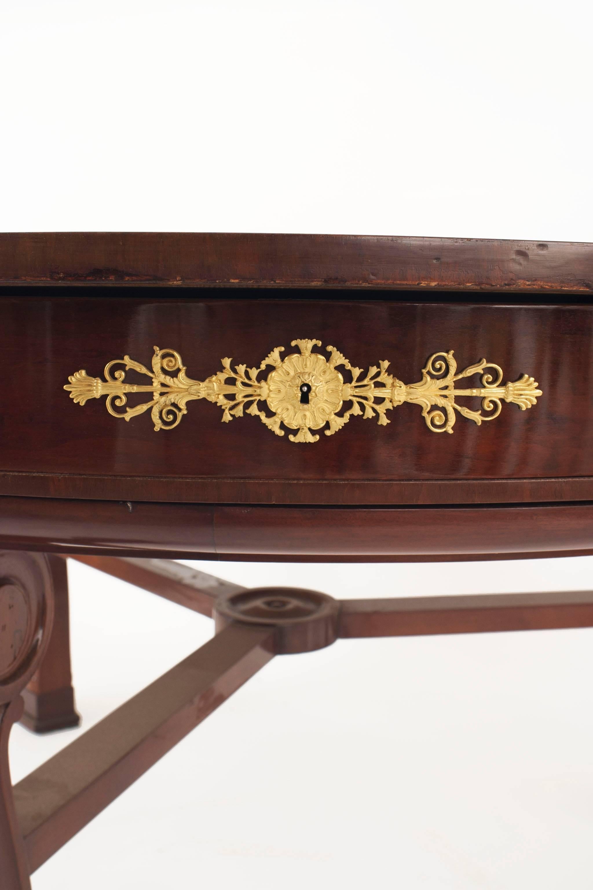 French Empire mahogany & gilt bronze trim round center table on 3 legs with a revolving inset brown leather top and pearl medallions over 6 drawers with a stretcher (stamped: POTHEAU).
