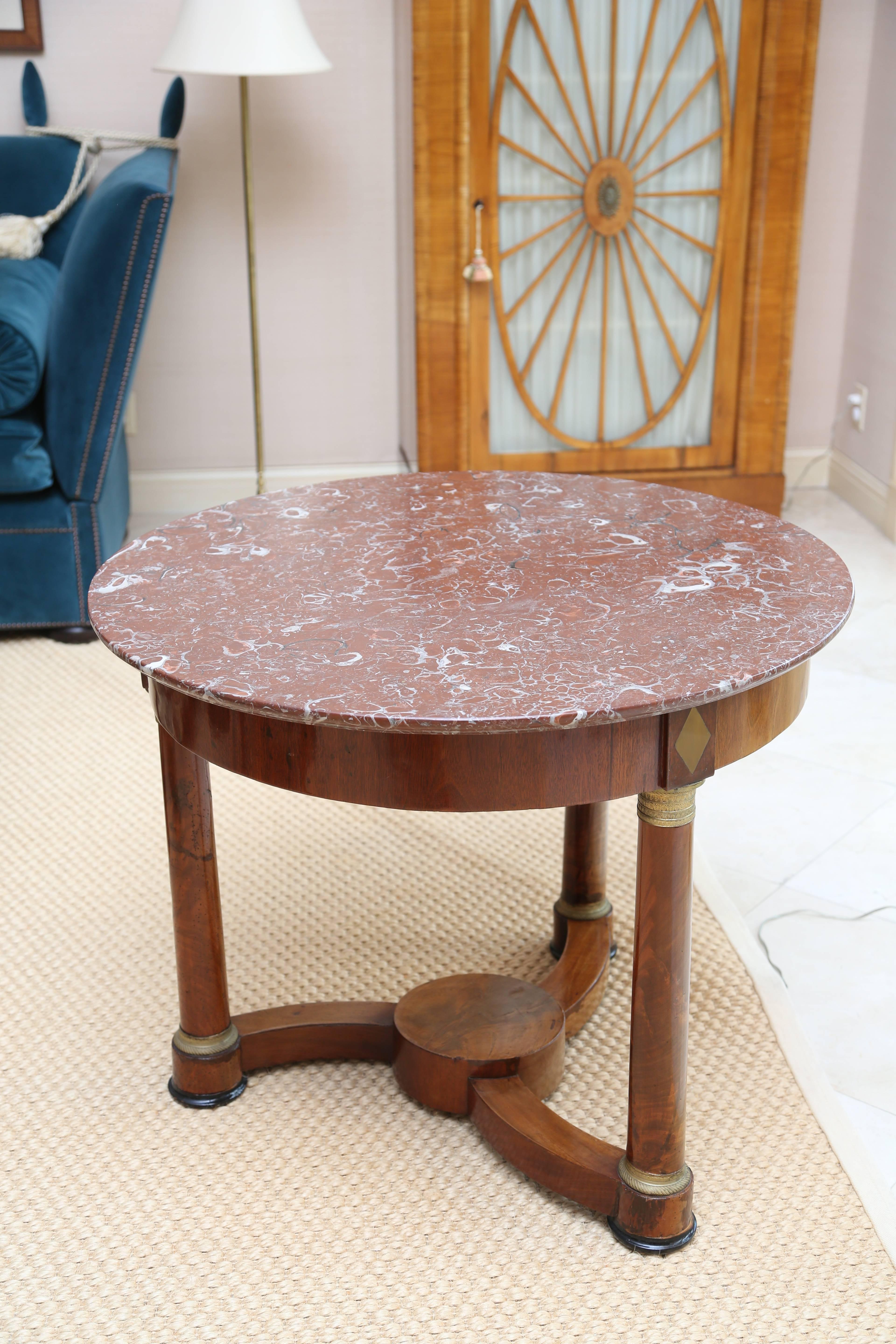 With round red fossil stone top over a frieze raised on three columnar supports with gilt metal capitals and bases headed by brass inlaid diamonds, joined by platform stretchers. Nice figure to mahogany.