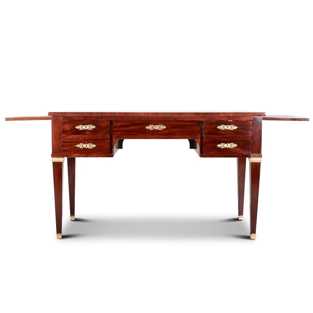 A fine, French Empire-style desk, the richly-figured mahogany timber contrasting smartly with finely-detailed gilt mounts and with a gilt-tooled leather top. Five fitted oak-lined drawers with hand-cut dovetail joinery and gilt bronze key