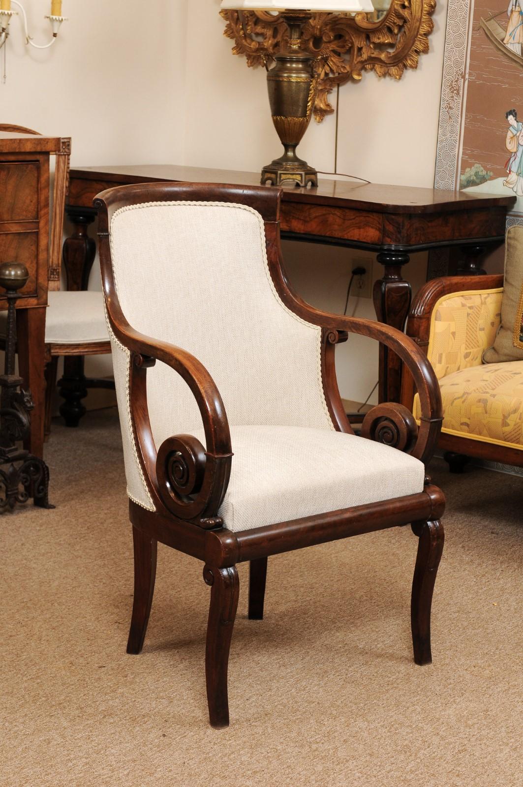 An early 19th century Empire mahogany fauteuil/armchair featuring rounded back, linen upholstery and scroll arms.
