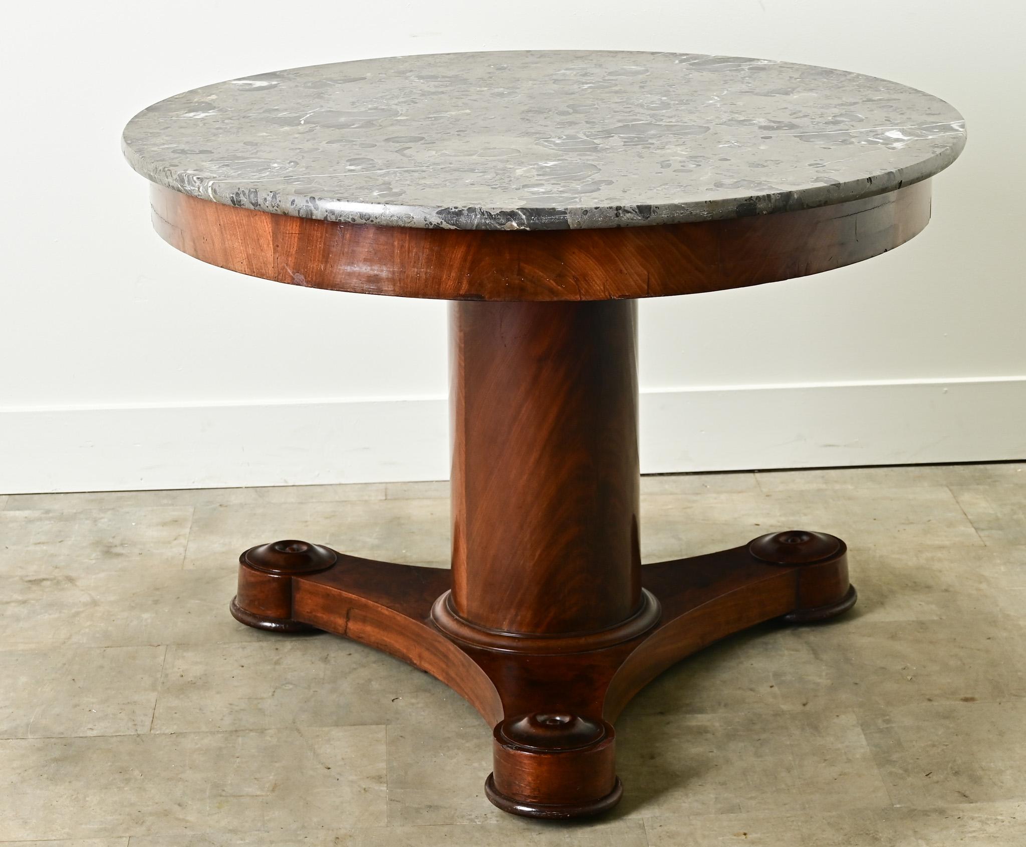 A large round center table from 1800’s France. The original marble top is worn and colorful over its refined mahogany base. A simple apron sits over a column form center pedestal over three concave splayed legs ending with rounded feet. Cleaned and