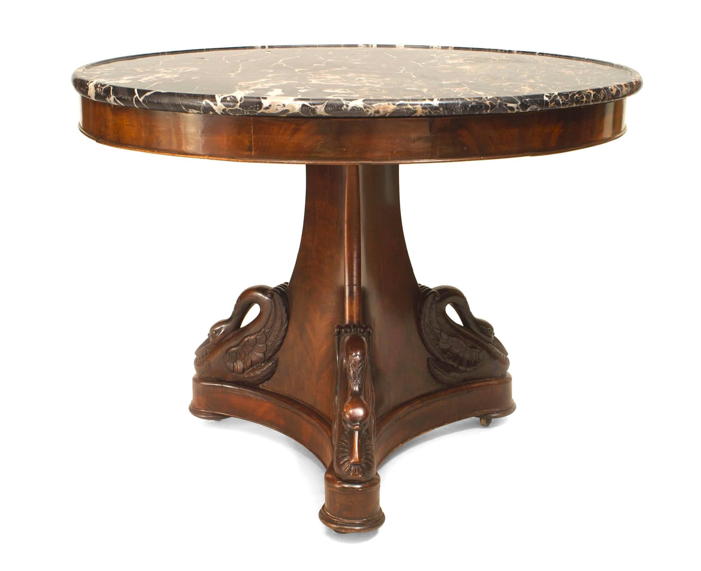 French Empire mahogany pedestal base center table with 3 carved swans on a base supporting a round black veined top with an molded edge.
