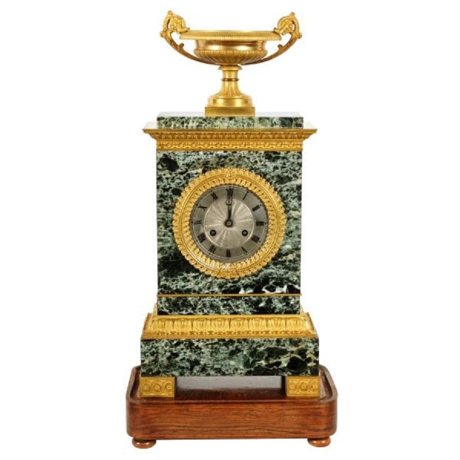 A 19th century French Empire design marble and ormolu table or mantel clock.

The clock has an eight day movement that strikes the hour and half hour on a bell and the pendulum is an early silk suspension.

The clock has a dark green with white