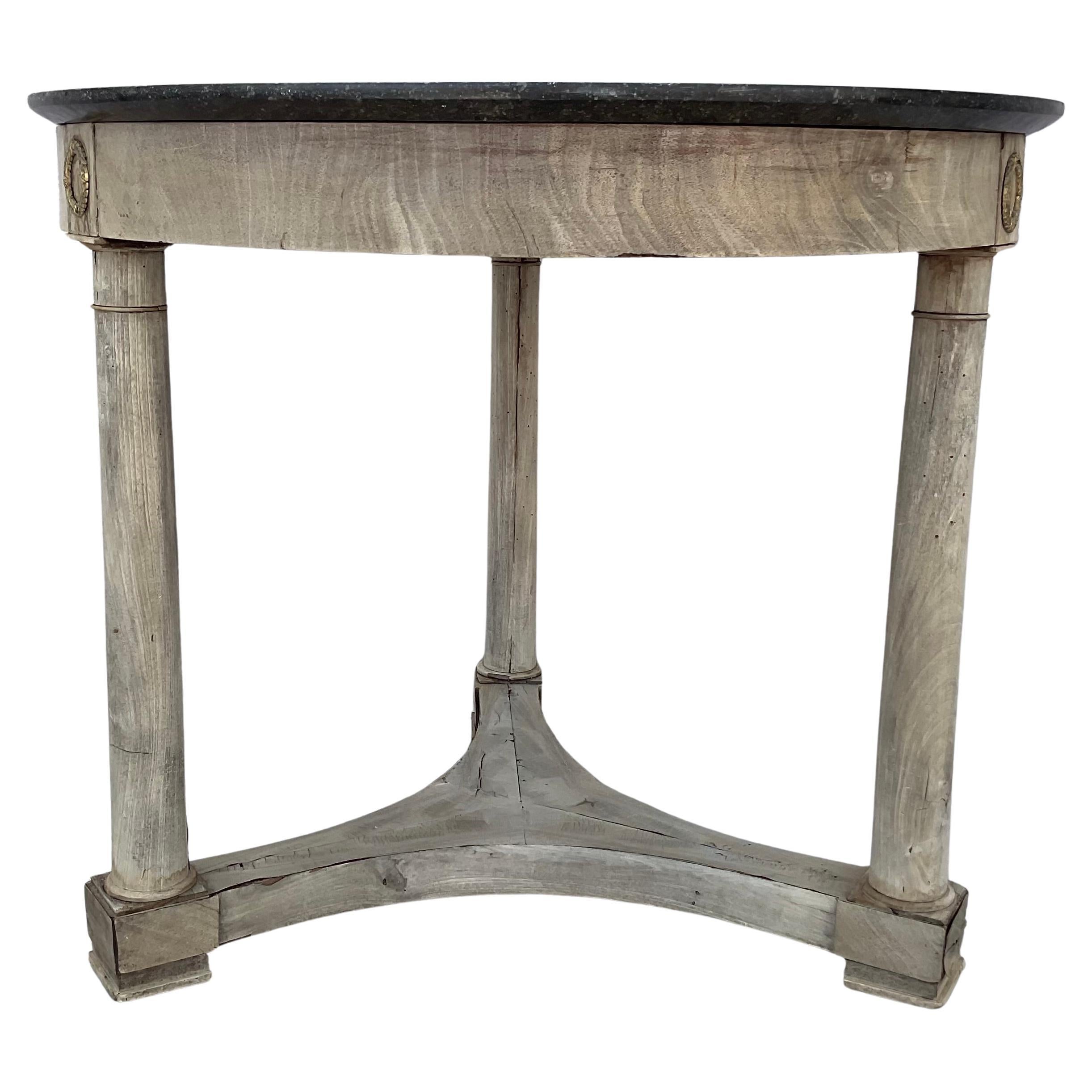 Early 19th century French Empire round black marble top over bleached mahogany base Center Table. Table features three column supports, applied bronze wreath mounts at joints, splayed base, all on three feet with castors. As a center table, it