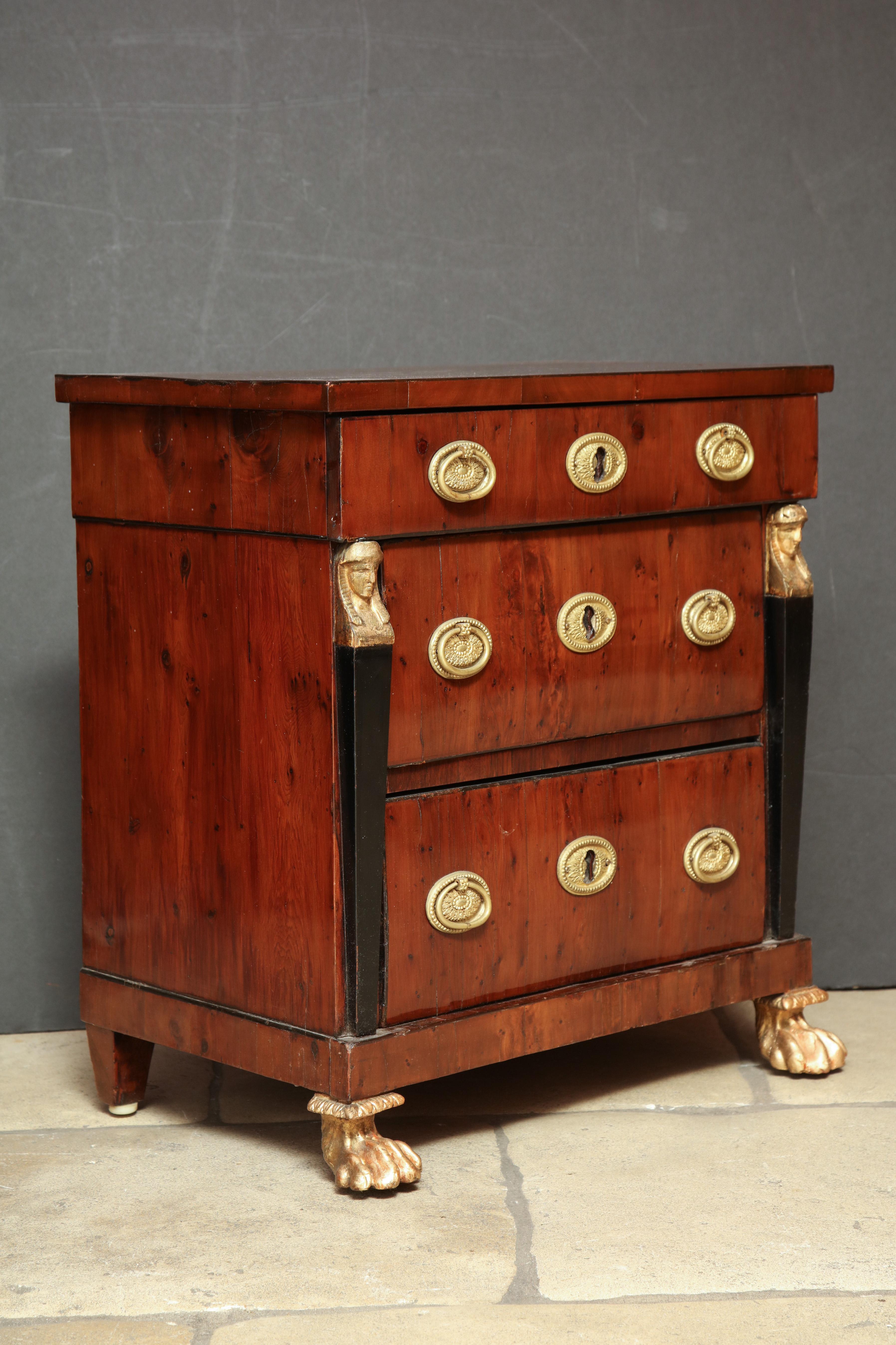 A fine French Empire mahogany three-drawer miniature commode with brass oval pulls, sphinx head capitals and carved gilt paw feet.