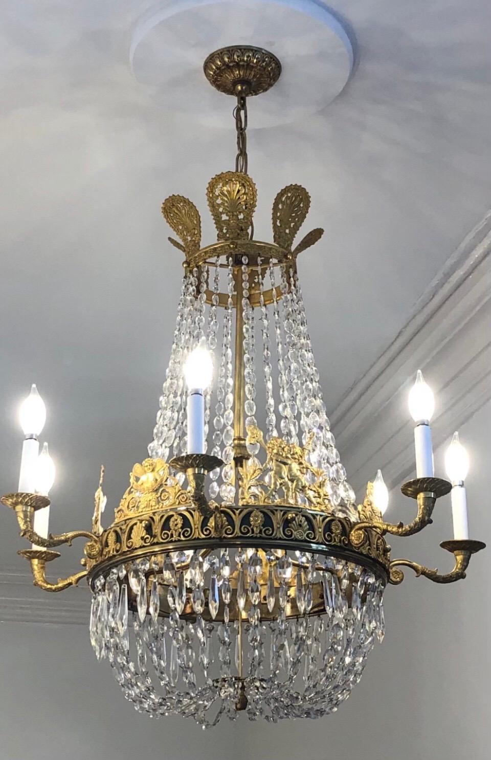 This Empire chandelier has a bronze Doré Corona above oval shaped crystal chains descending to Doré mounted circular dark green painted bronze band with seven candelabra arms and terminating in an elegant crystal chain basket.