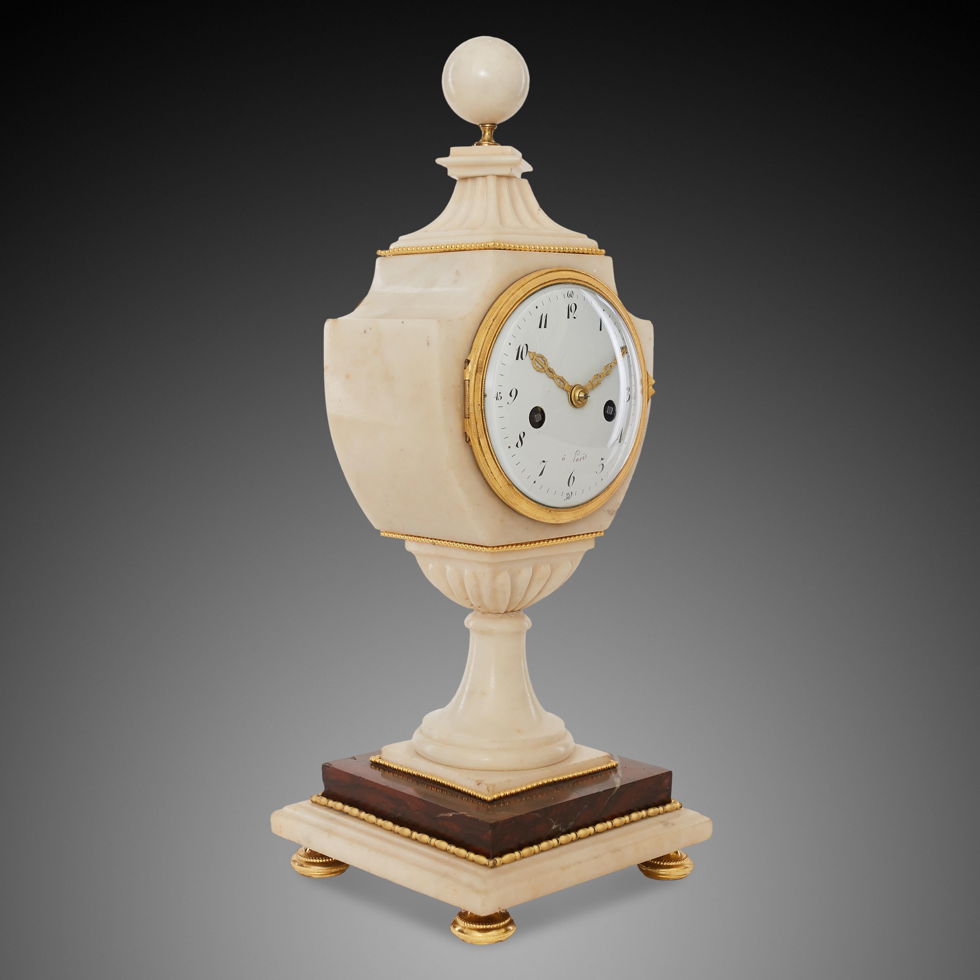 Cette horloge de cheminée ancienne a été créée à Paris à la fin du XVIIIe siècle. Le corps principal de la pendule de cheminée est en marbre blanc et le socle est constitué d'un fragment de marbre rouge Napoléon, ce qui confère à la pendule de