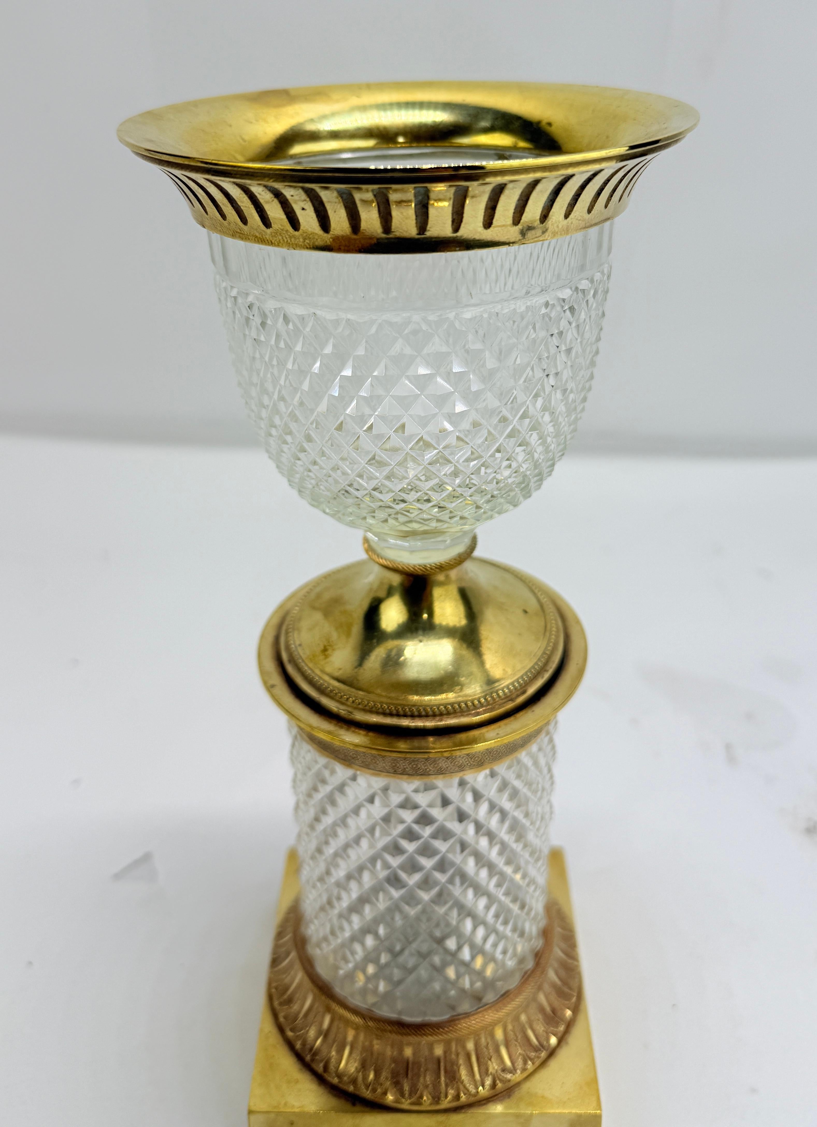Un élégant vase à pot-pourri de petite taille de l'Empire français, finement monté en bronze doré au feu (ormolu) et en cristal richement taillé. Le récipient est disposé en deux étapes : au-dessus, une coupe en cristal en forme de coupe avec une