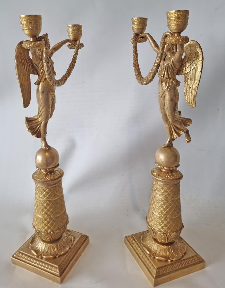 Un'impressionante coppia di candelabri in ormolu dell'Impero francese dell'inizio del XIX secolo, a forma di figure alate di dame in piedi, che tengono in alto ugelli decorati con teste di fiori, legati da ghirlande floreali e nastri, montati su