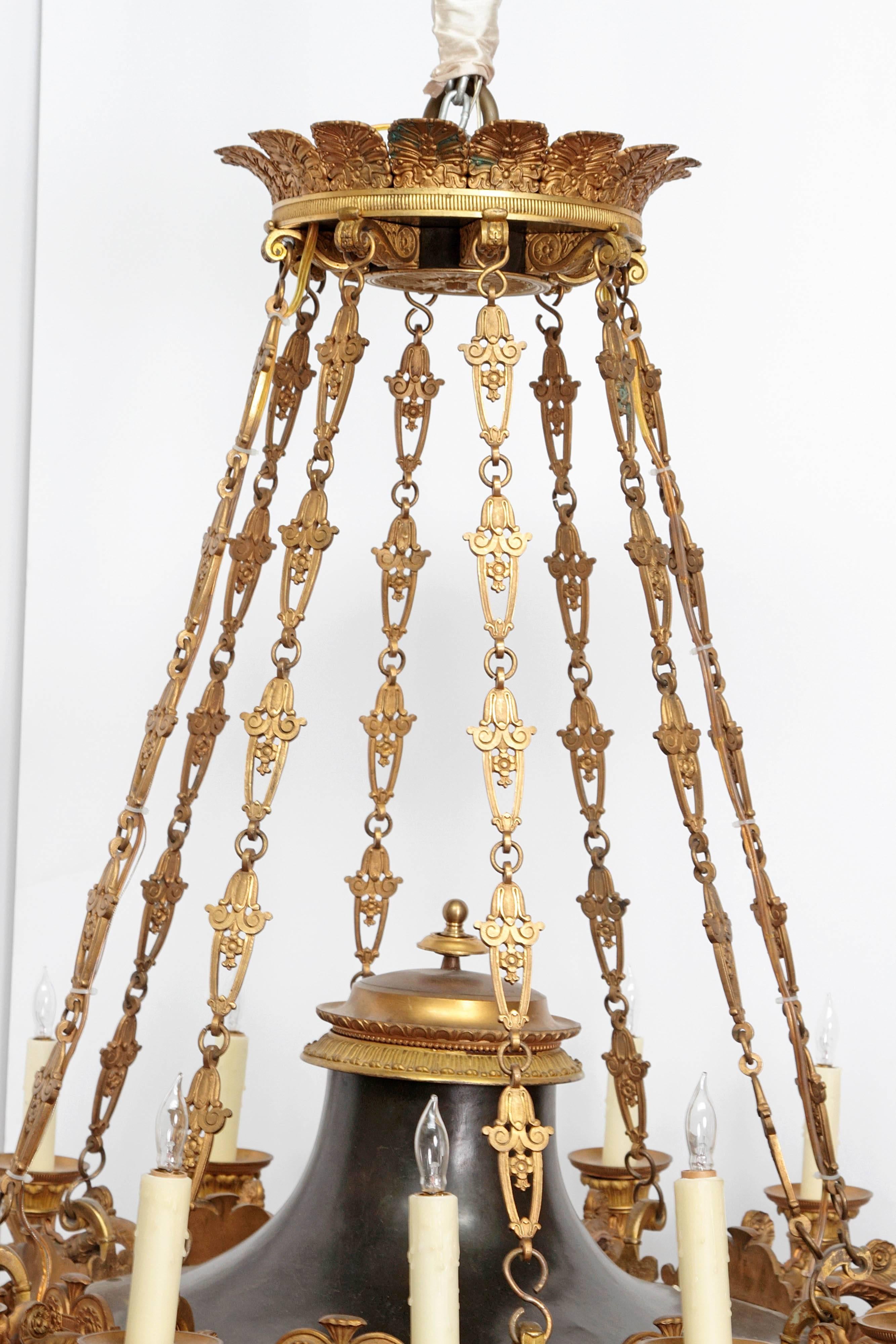 A large French Empire patinated and gilt bronze argon chandelier with 16 lights. Crown as top with palmette motif. Hanging chains supporting black disc forms with decorative trim holding lights. Centre pendant at bottom, early 19th century, France.