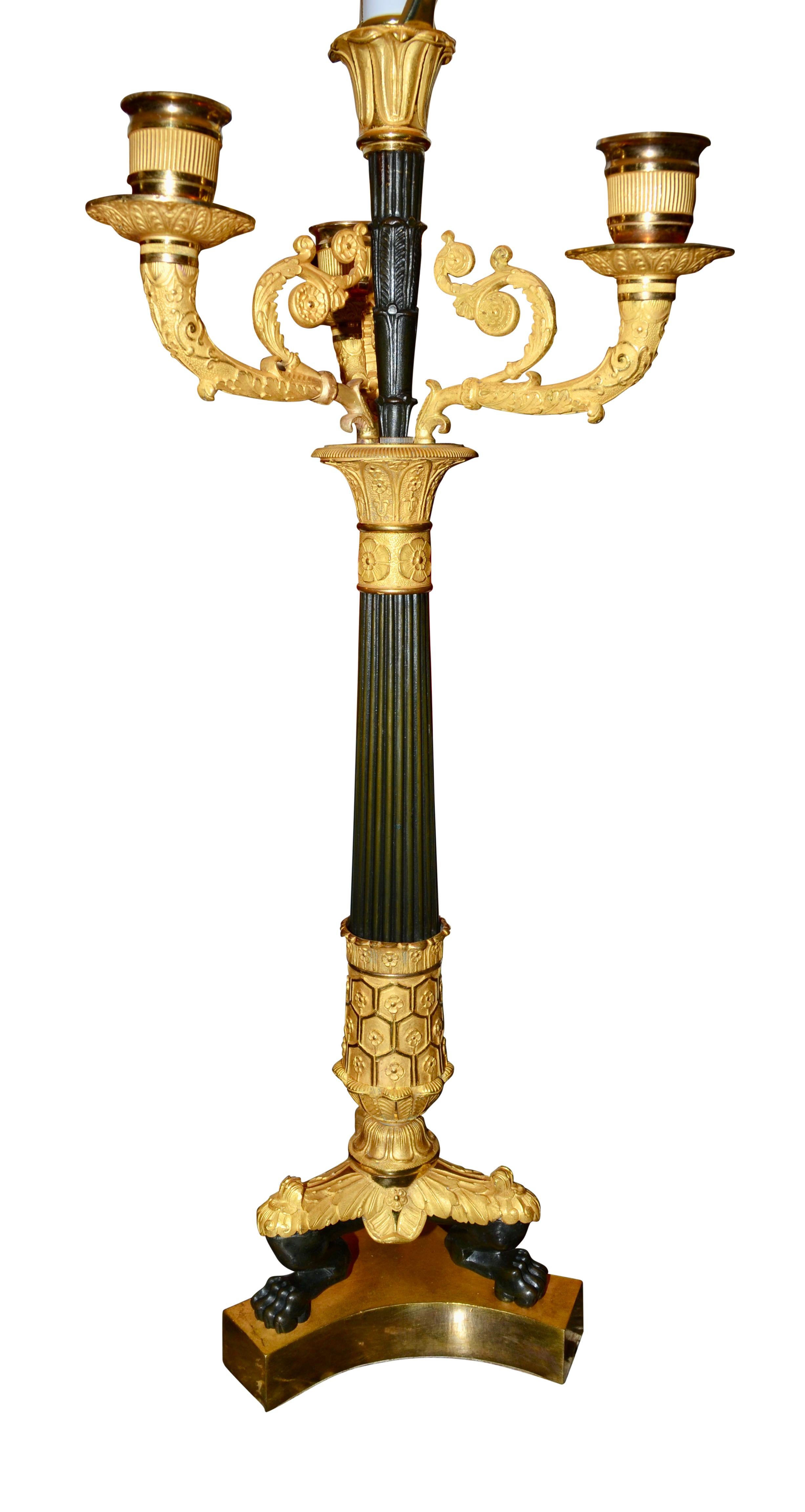 A finely chased and gilded period French Empire candlestick that has been electrified. The triform gilded bottom supports three patinated lions paw feet with gilded tops which connect to a patinated and gilded bronze central stem, the top of which