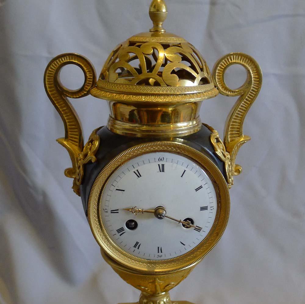 French Empire patinated bronze and ormolu vase clock. Of unusual design set as it is on a spread ormolu base of eight sides, the front and back being long sides. The base sits upon four fine ormolu bun feet decorated with hatching. To the centre of