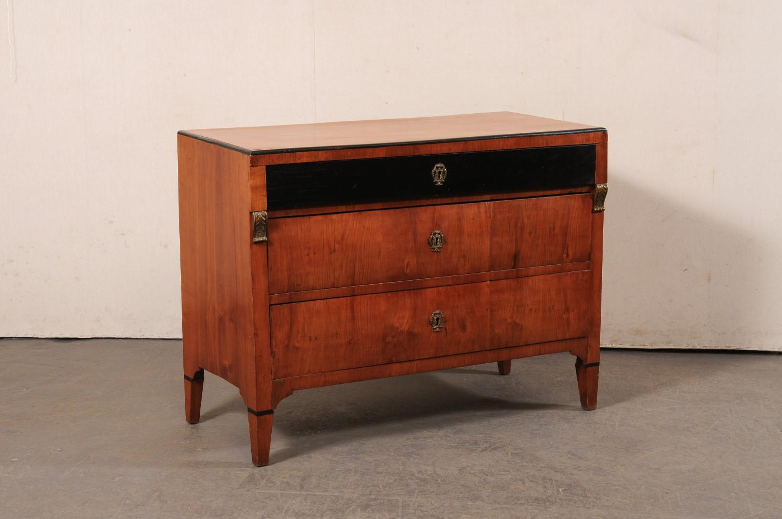 A French Empire period commode, with black and brass accents, from the early 19th century. This antique chest from France features a rectangular-shaped top, with case which houses three graduated drawers, with upper drawers flanked within front side