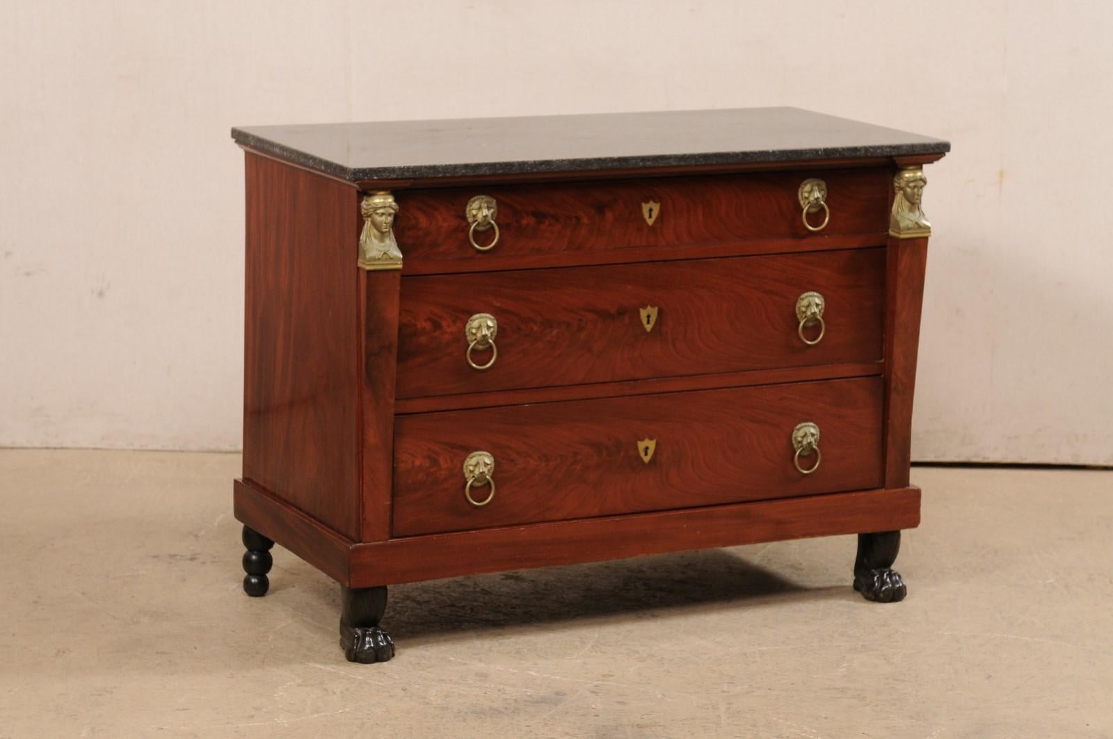 A French Empire period wooden commode, with marble top and revival accents, from the early 19th century. This antique commode from France features a rectangular-shaped black marble top, above a case which houses three drawers and is designed with